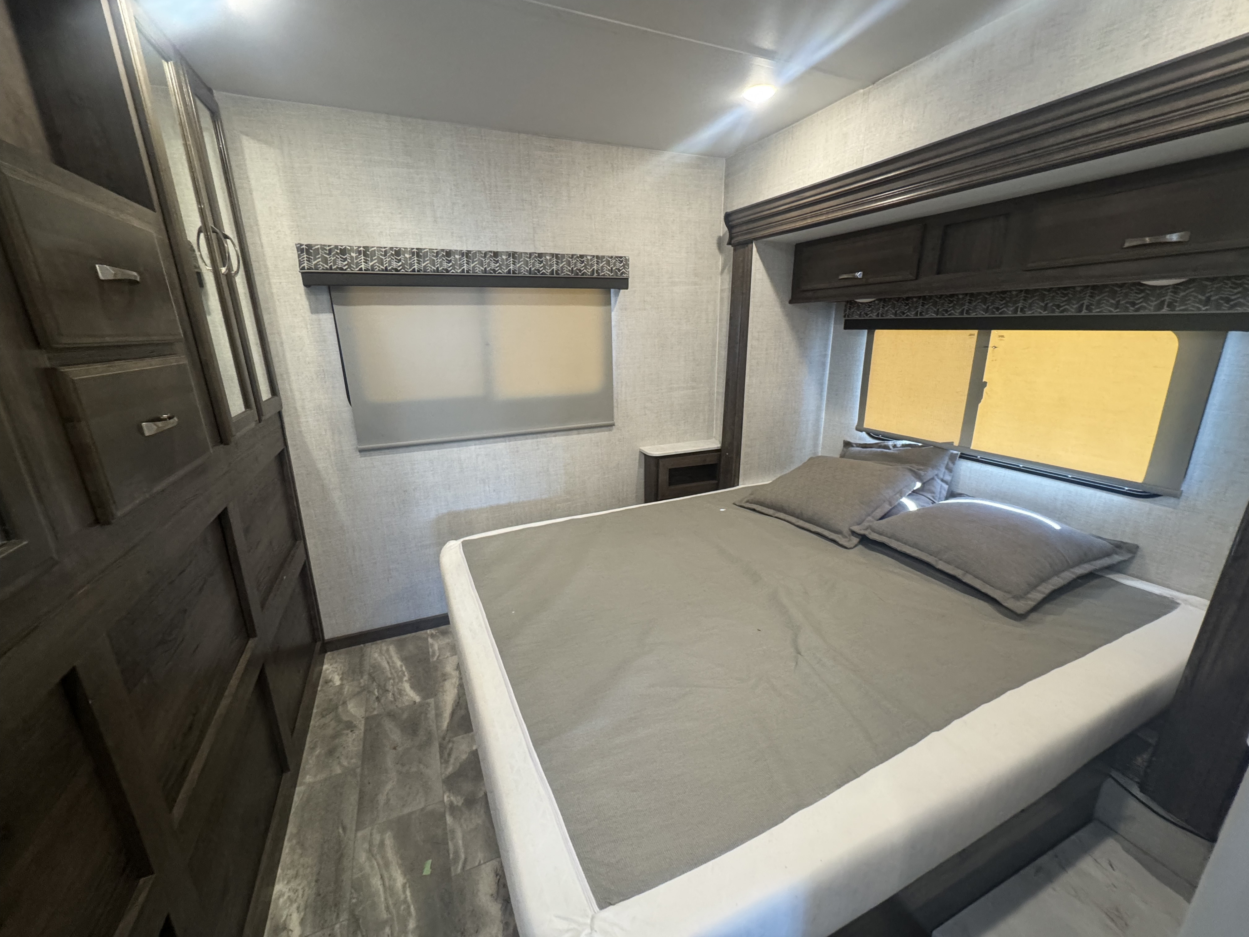 Comfortable RV rental bedroom with modern grey bedding, ample dark wood storage, and warm lighting, perfect for travel.. Gulf Stream 6314 2023