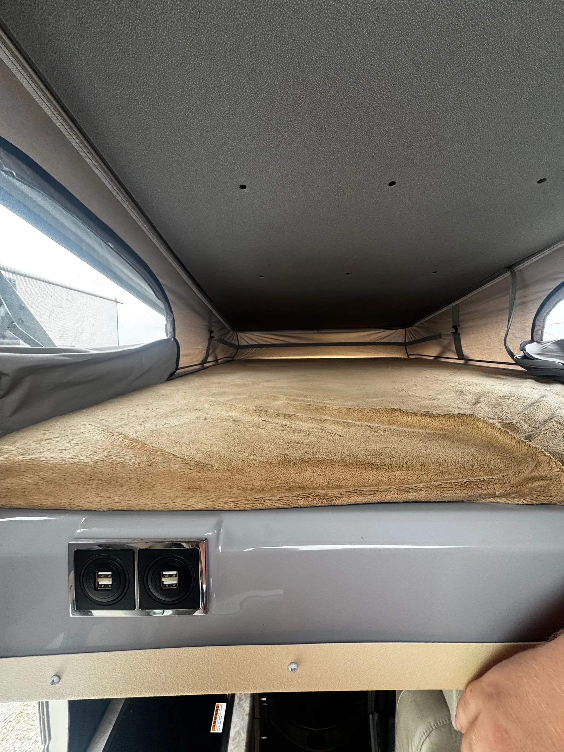 Cozy pop-top RV rental sleeping area: tan bed, mesh windows, and handy USB charging ports for your next adventure.. Thor Scope 2023