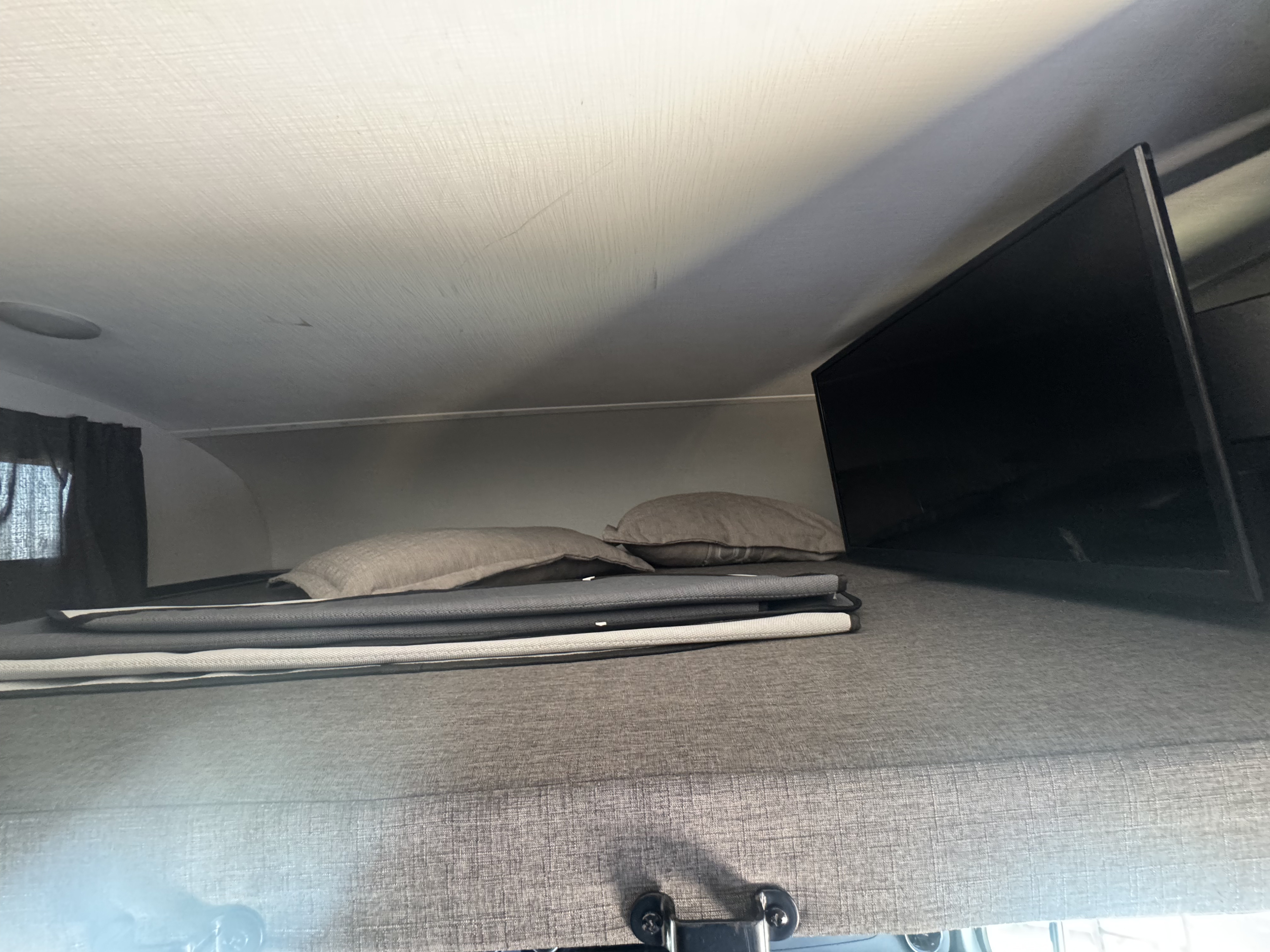 Overhead sleeping area in an RV rental, featuring a bed, pillows, and a TV for compact comfort.. Forest River Sunseeker MBS 2023
