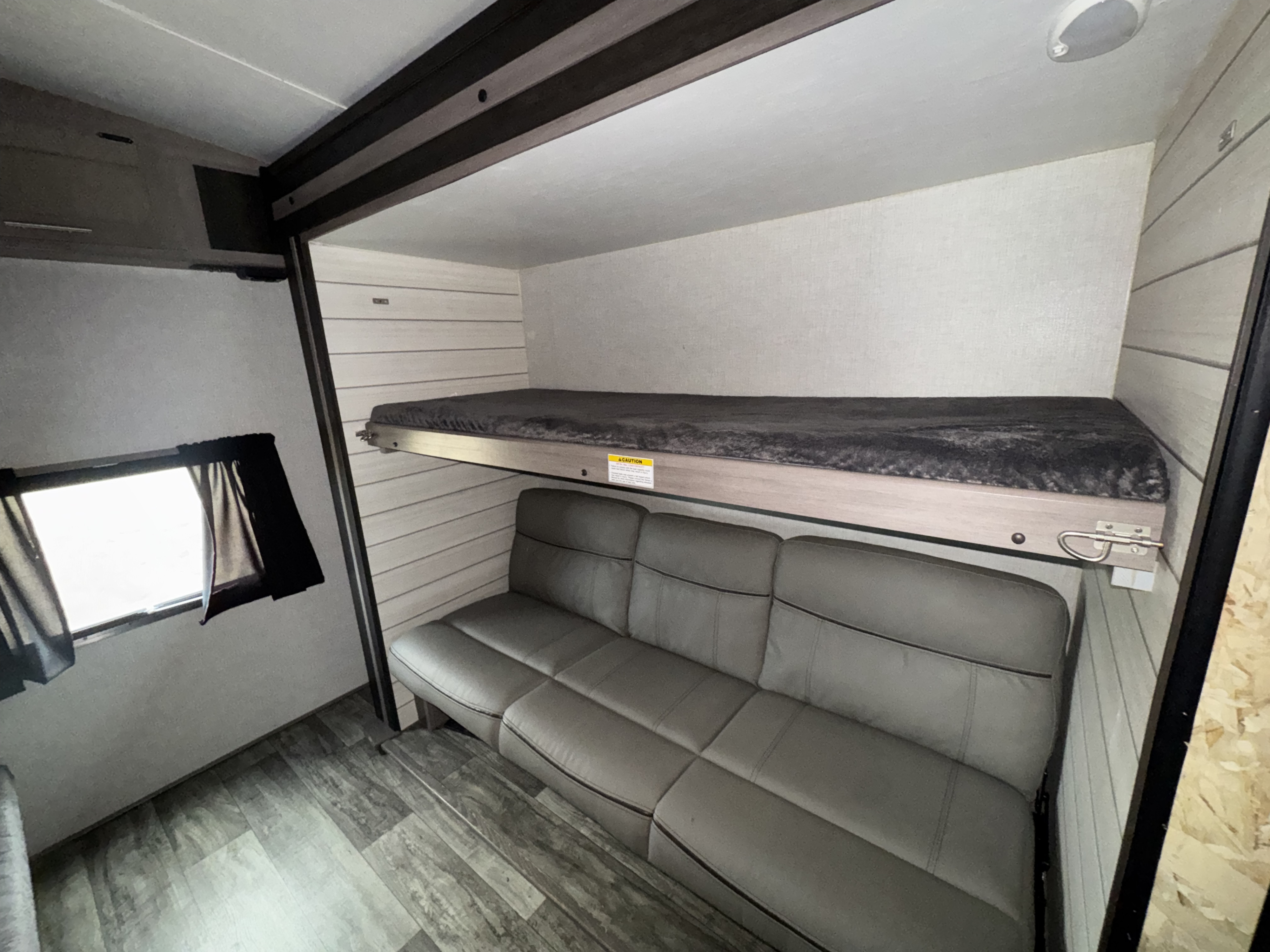 Cozy RV rental interior featuring a bunk bed above a gray sofa, with wood-look flooring and a small window.. Crossroads RV Sunset Trail Super Lite 2022