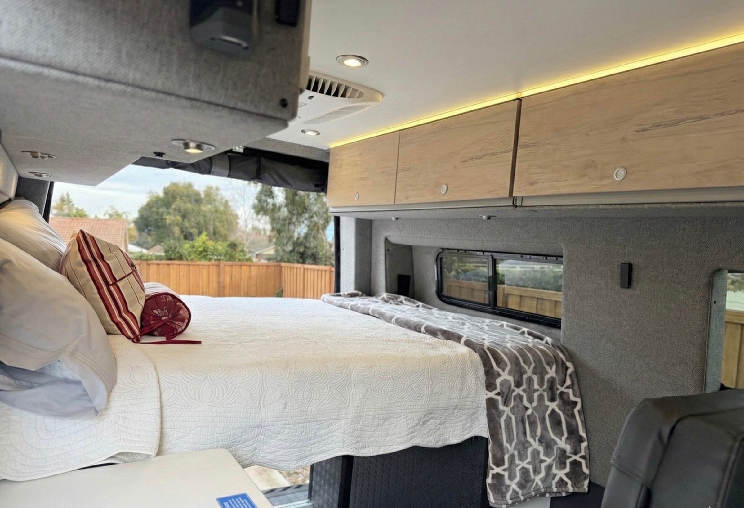 Inviting RV rental interior: a comfy bedroom with storage, ambient lighting, AC, and a scenic window view.. Mercedes Sprinter Motorhome Campervan RV 2025