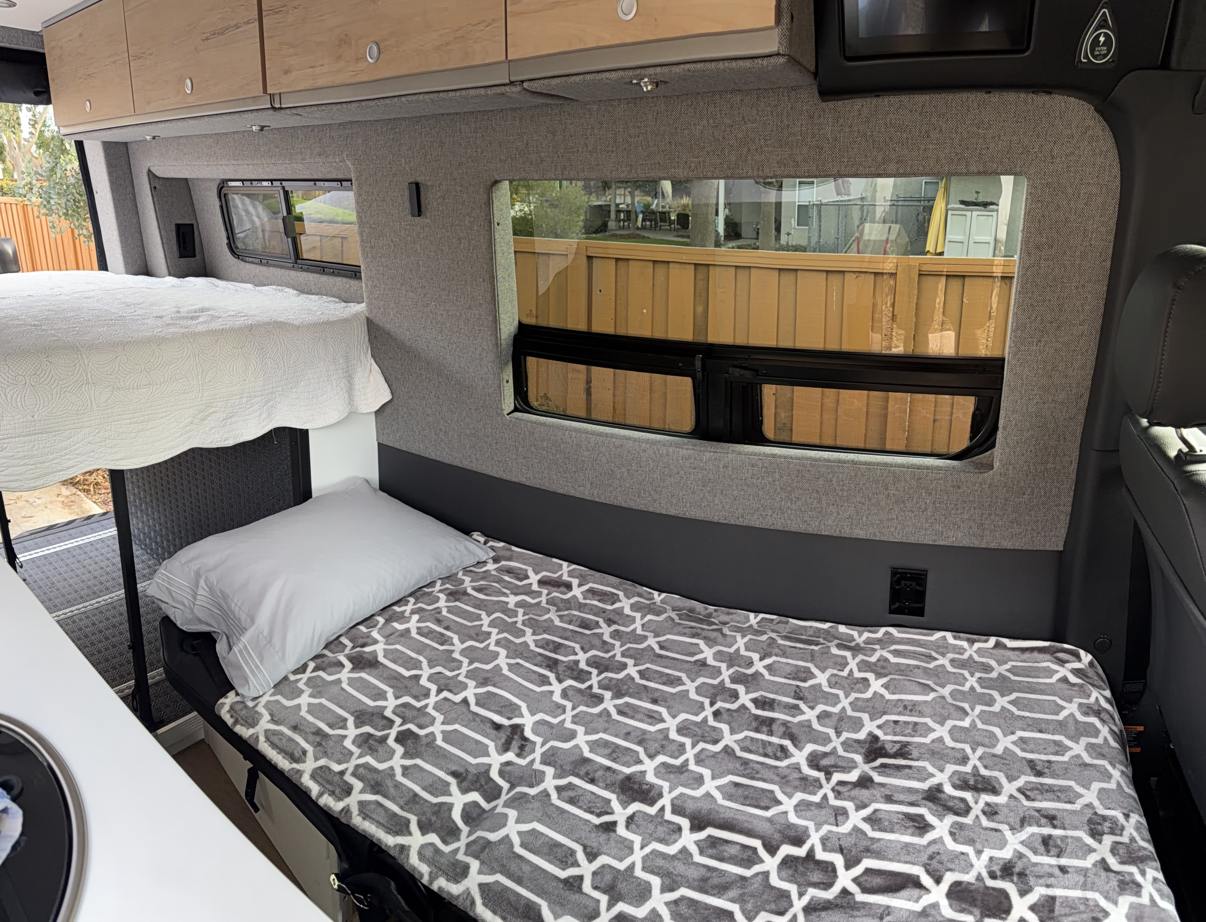 Cozy RV rental interior with bunk beds, wooden cabinets, and windows offering outdoor views. Perfect for camper van adventures.. Mercedes Sprinter Motorhome Campervan RV 2025