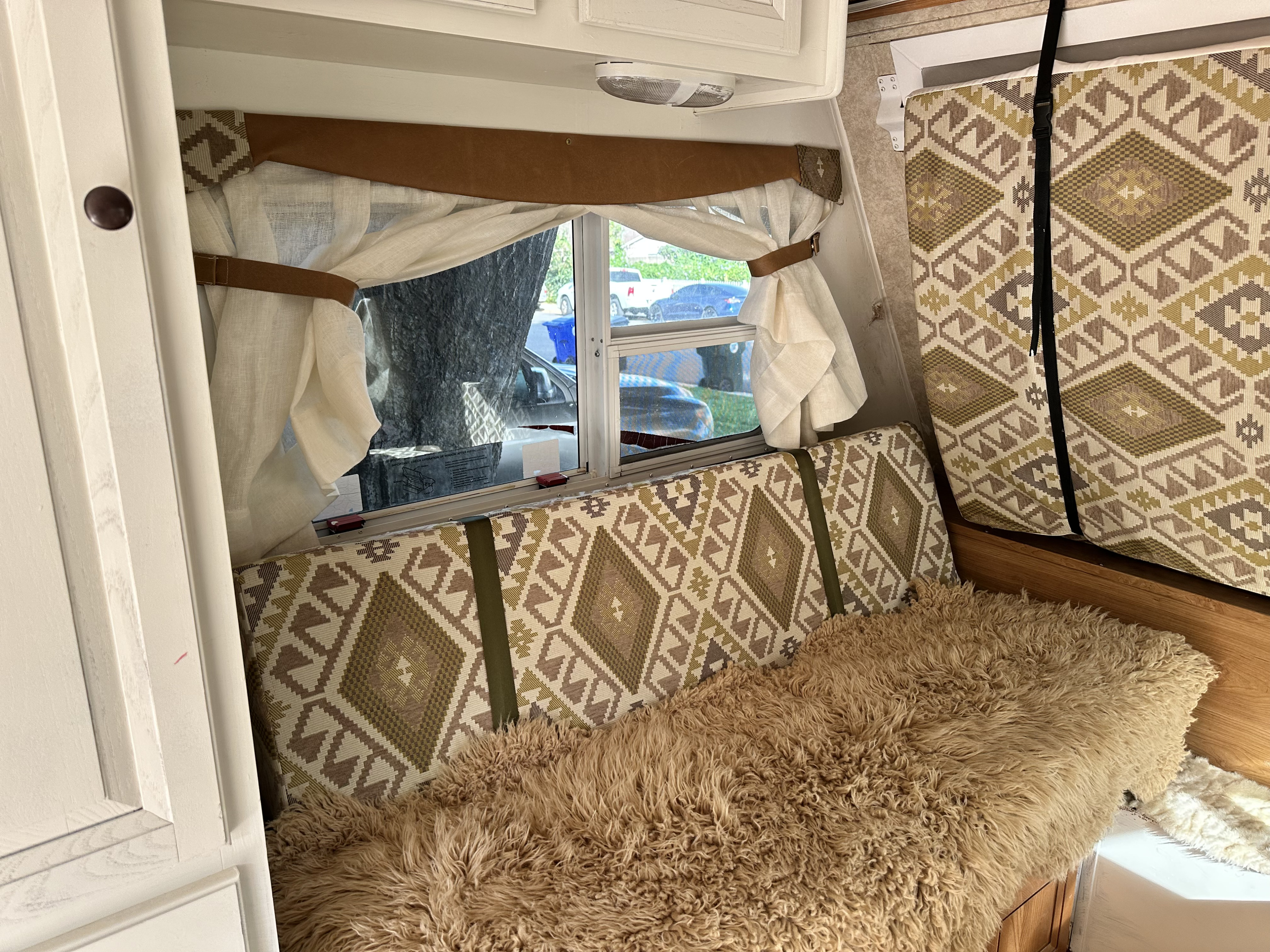 Cozy RV rental interior featuring patterned cushions, a furry throw, and tied-back curtains next to a window view.. Palomino Banshee 2011
