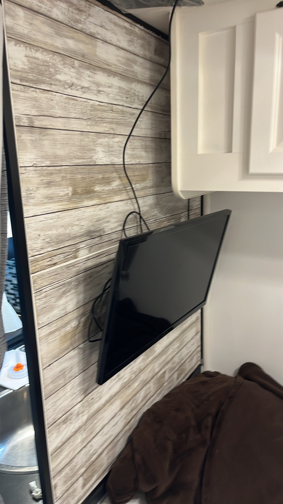 Cozy rv rental interior with wall-mounted TV on wood-look paneling, white cabinets, and a soft brown blanket.. Thor Majestic 2015