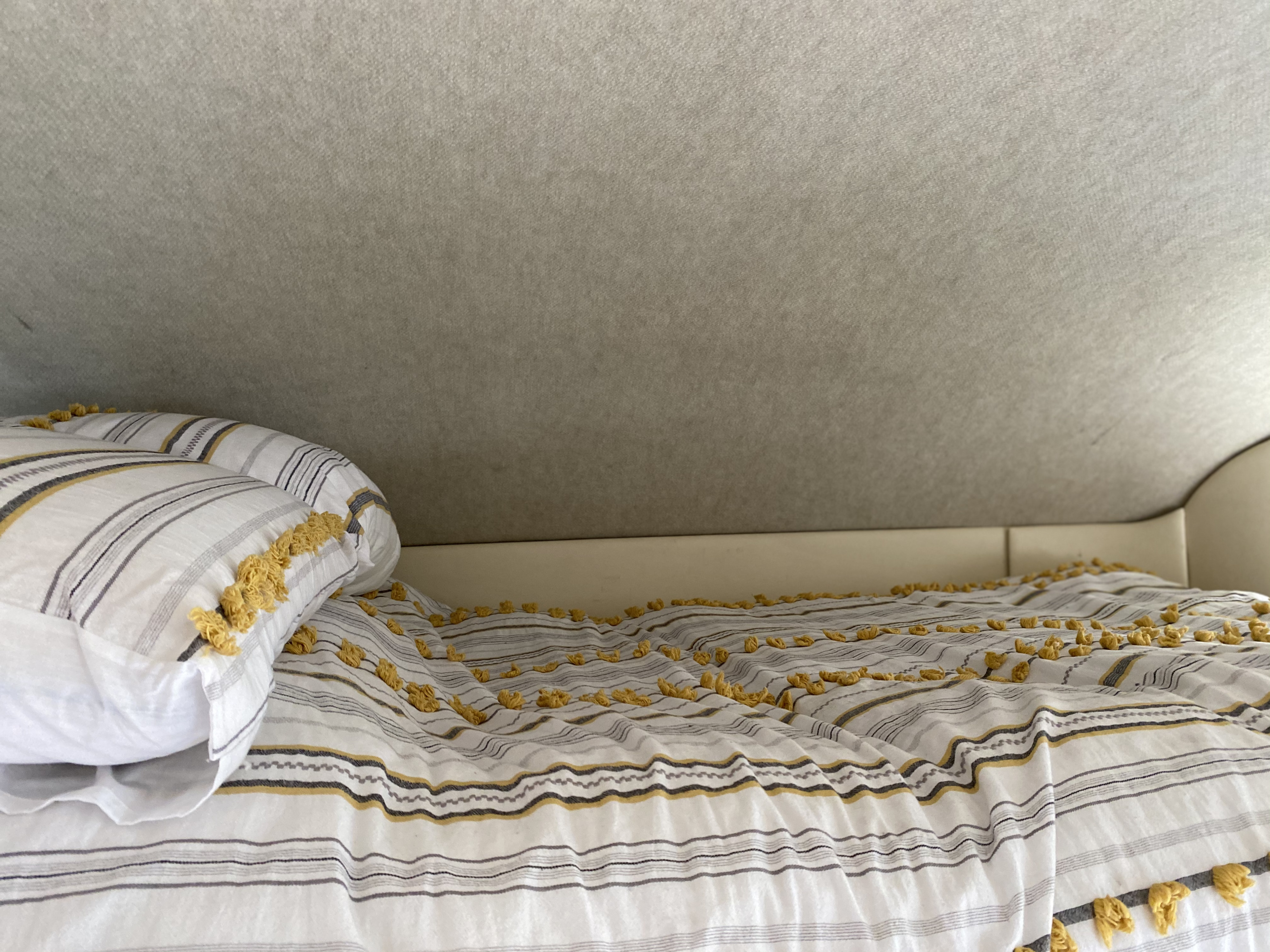 Comfortable bed inside an RV rental, featuring white, gray, and yellow striped bedding with charming yellow tufts.. Fleetwood Pulse 2008