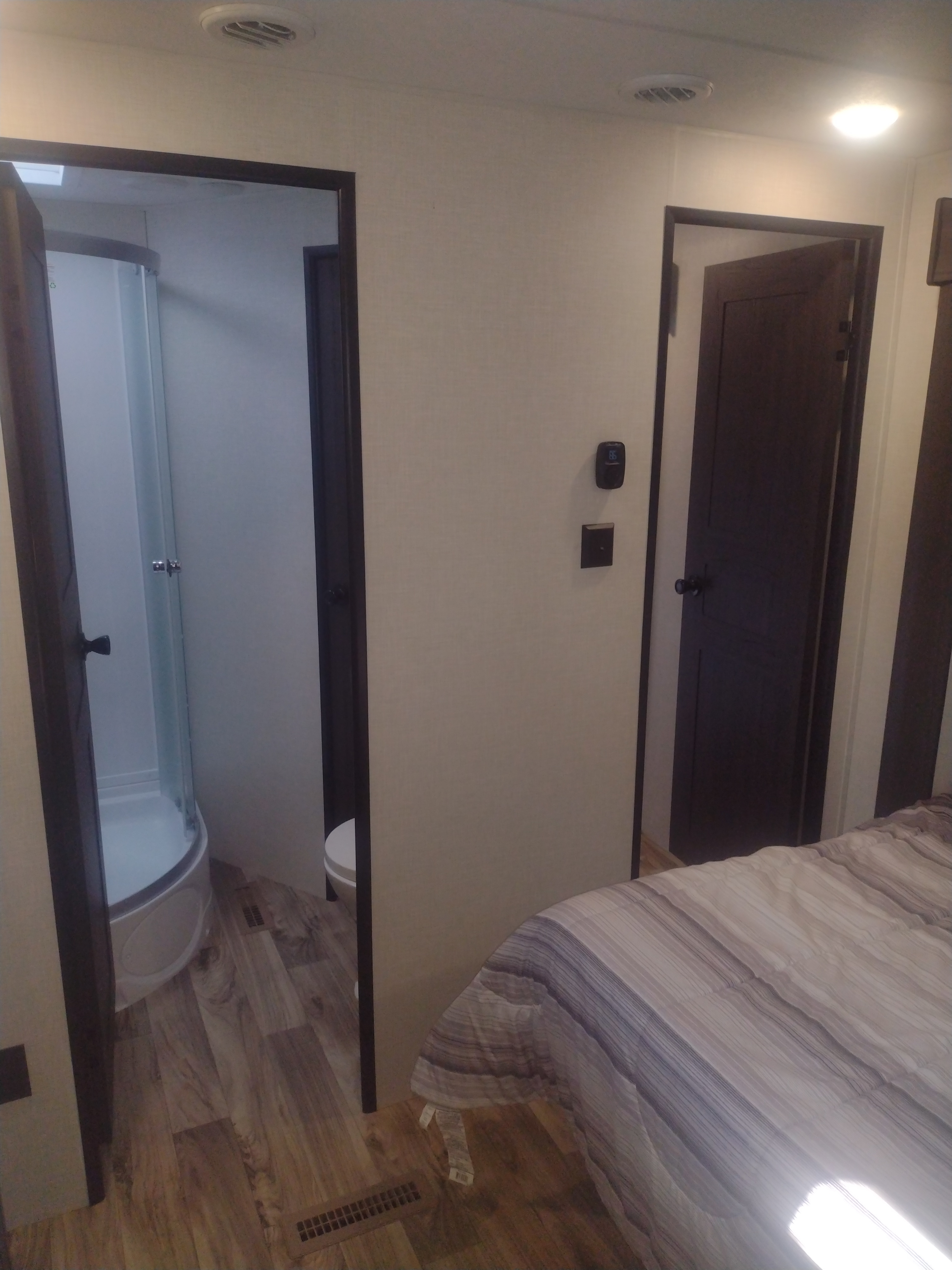 This RV rental interior features a cozy bedroom with a striped bed and two doors, one revealing a compact shower and toilet.. Sporttrek Touring Edition 2024