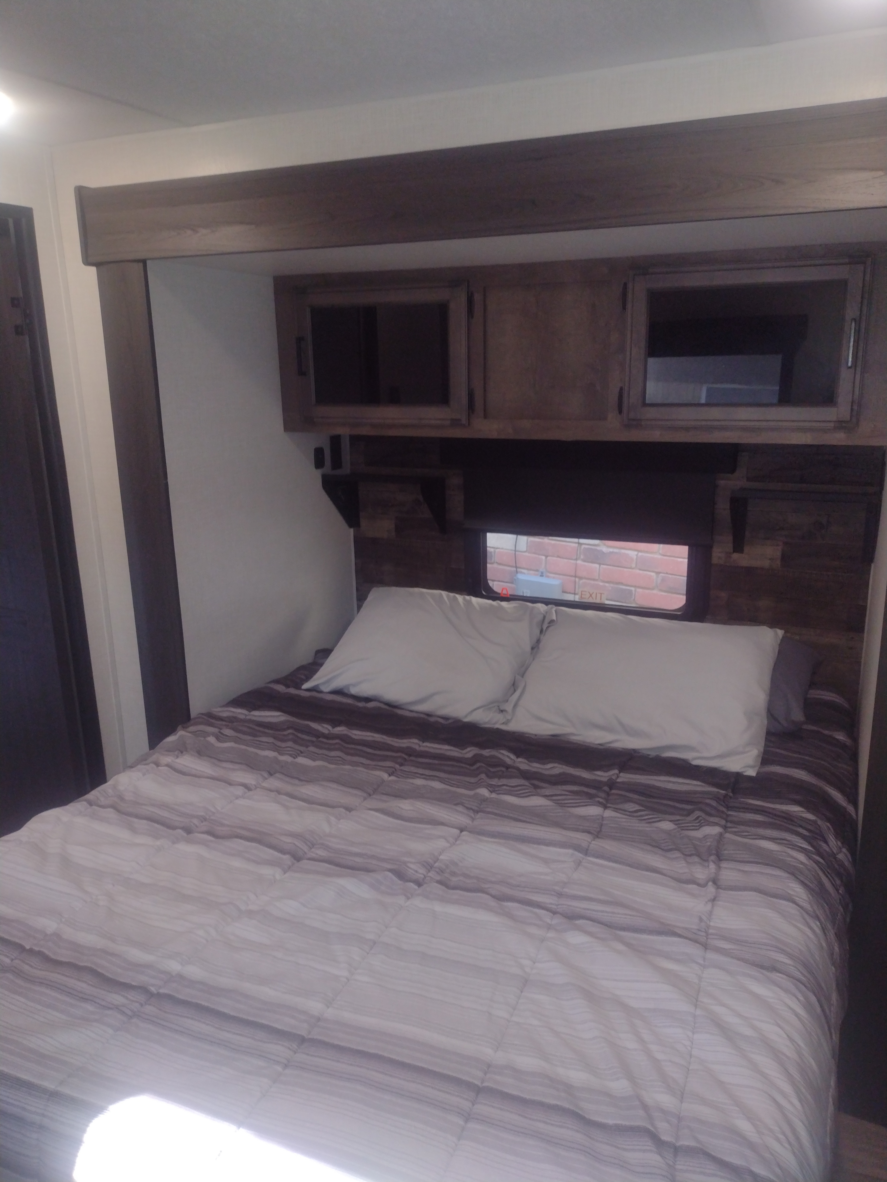 Relaxing RV rental bedroom featuring a striped bedspread, white pillows, overhead cabinets, and a window.. Sporttrek Touring Edition 2024