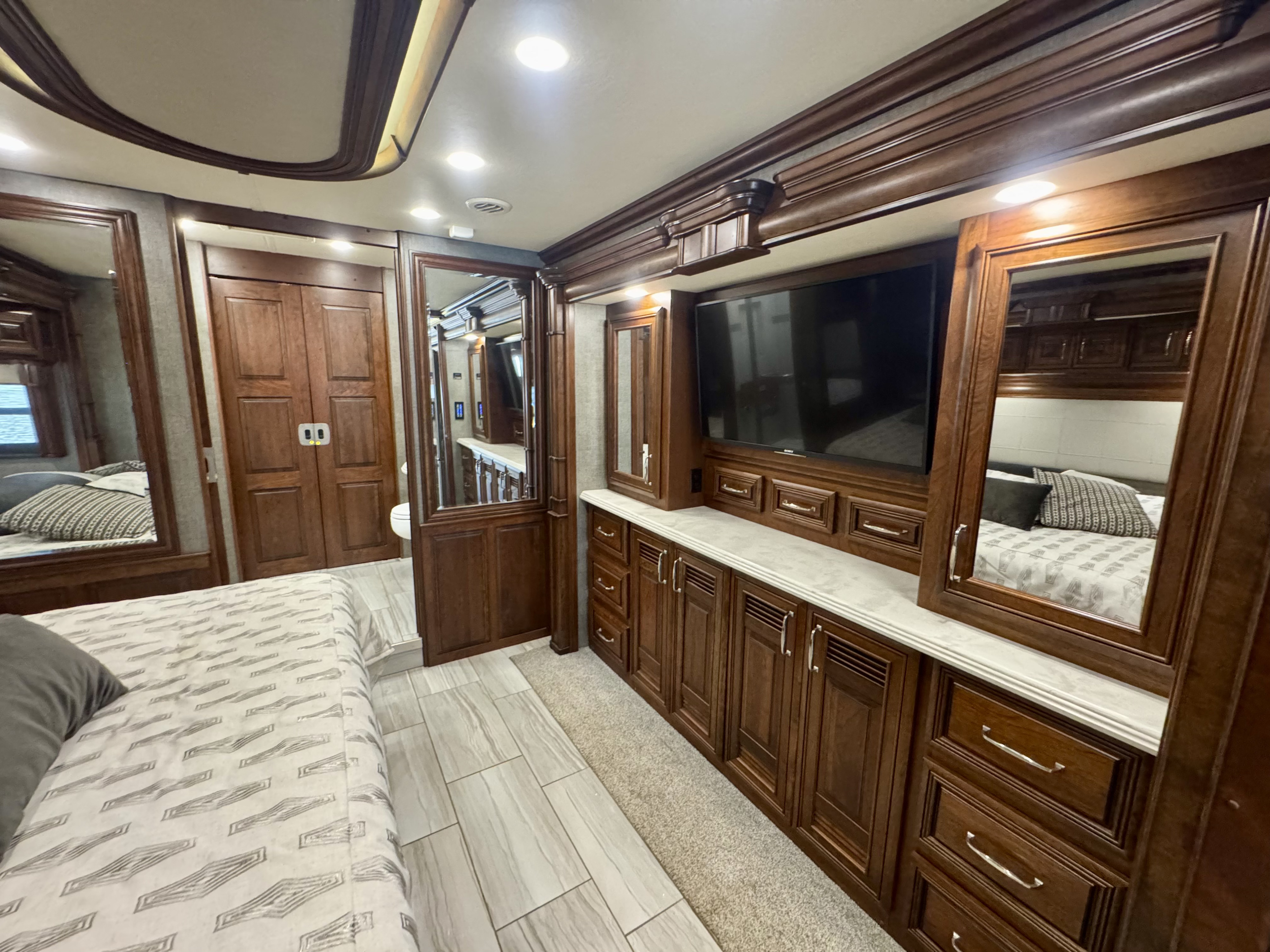 Luxurious RV rental bedroom with rich wood cabinetry, a large TV, patterned bed, and light tile flooring.. American Dream American Dream Motorhome 2019