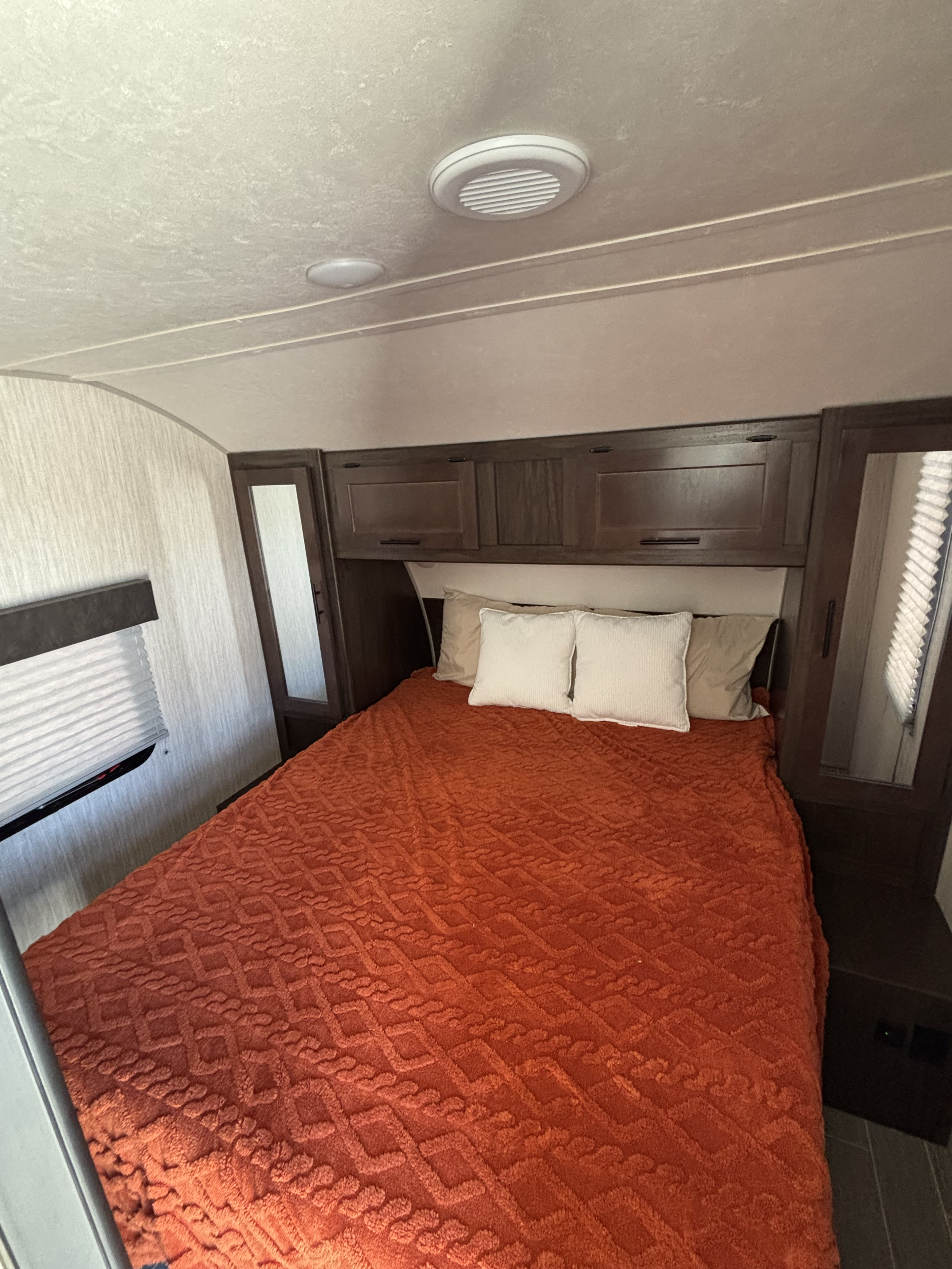 RV rental bedroom featuring a comfy bed with an orange blanket & pillows, overhead cabinets, and window. Ideal for travel.. Forest River Cherokee Grey Wolf 2021