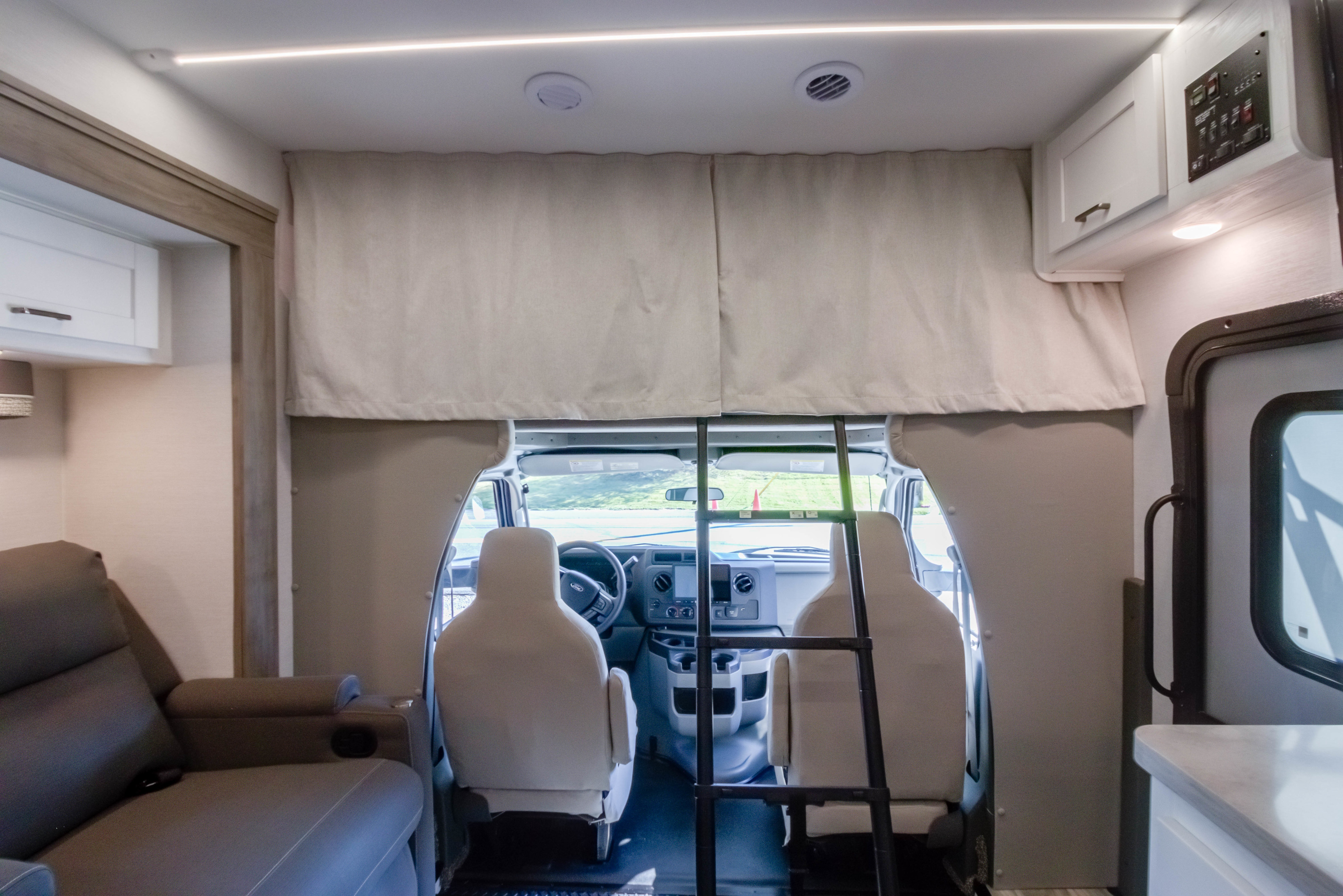 Inside this RV rental, view from the living area towards the cockpit, revealing front seats, ladder to a bunk, and functional controls.. gulf stream Conquest 2026