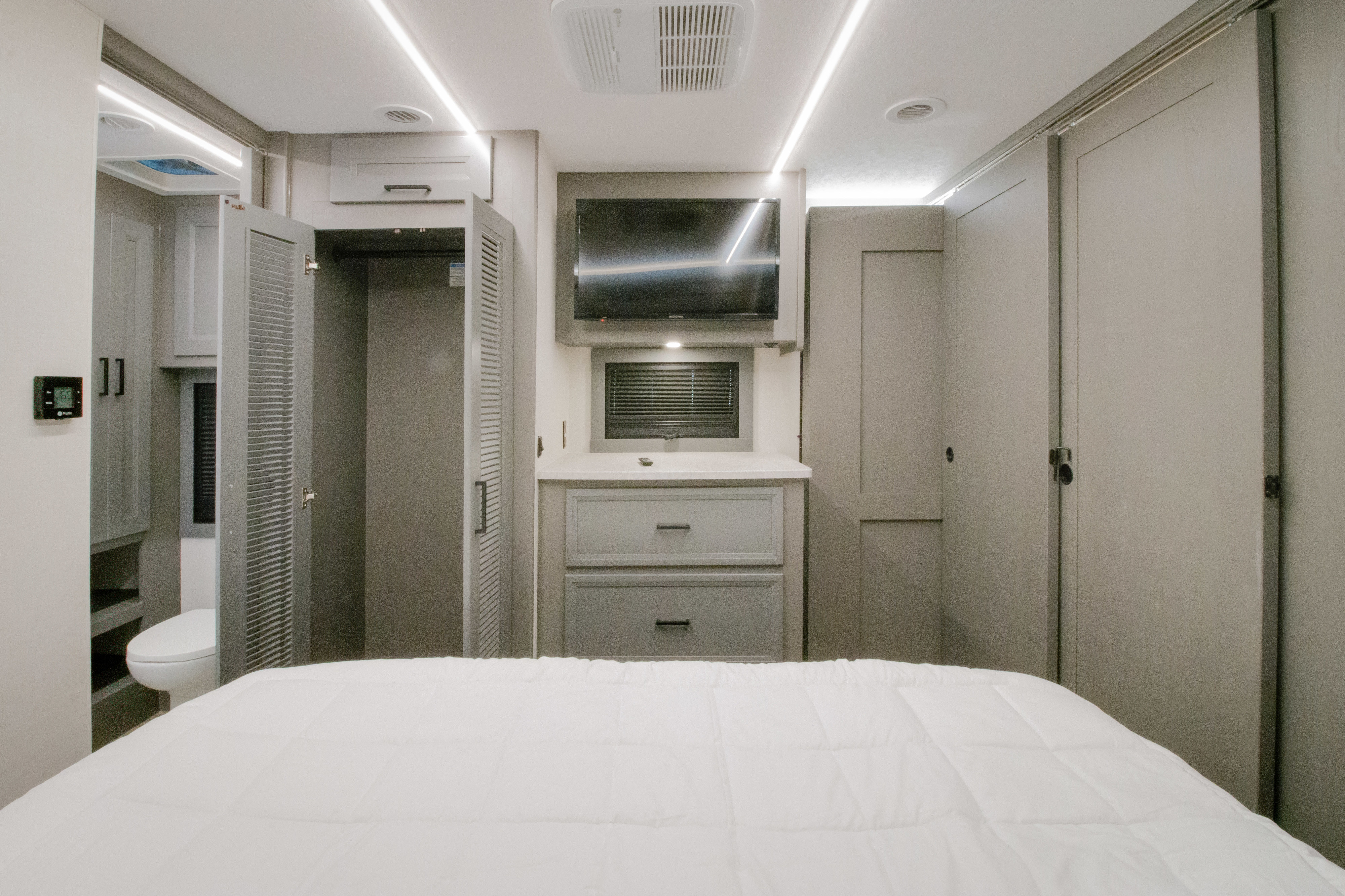 Comfortable RV rental bedroom featuring a white bed, TV, built-in storage, and a glimpse of the private bathroom, perfect for travel.. Forest River Coachmen Mirada 2026