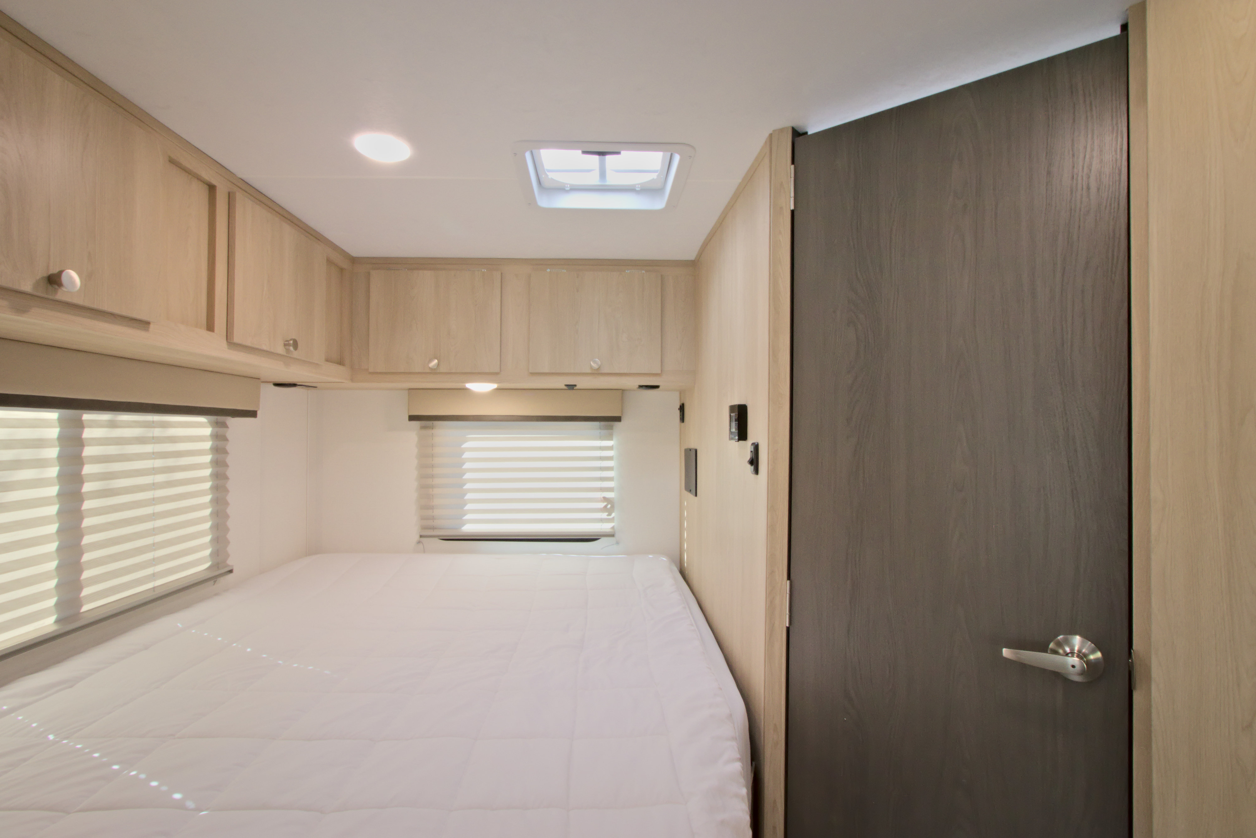 Experience comfort in this RV rental bedroom. Features a cozy bed, window blinds, light wood cabinets, and ample lighting.. Forest River Coachmen Leprechaun 2026