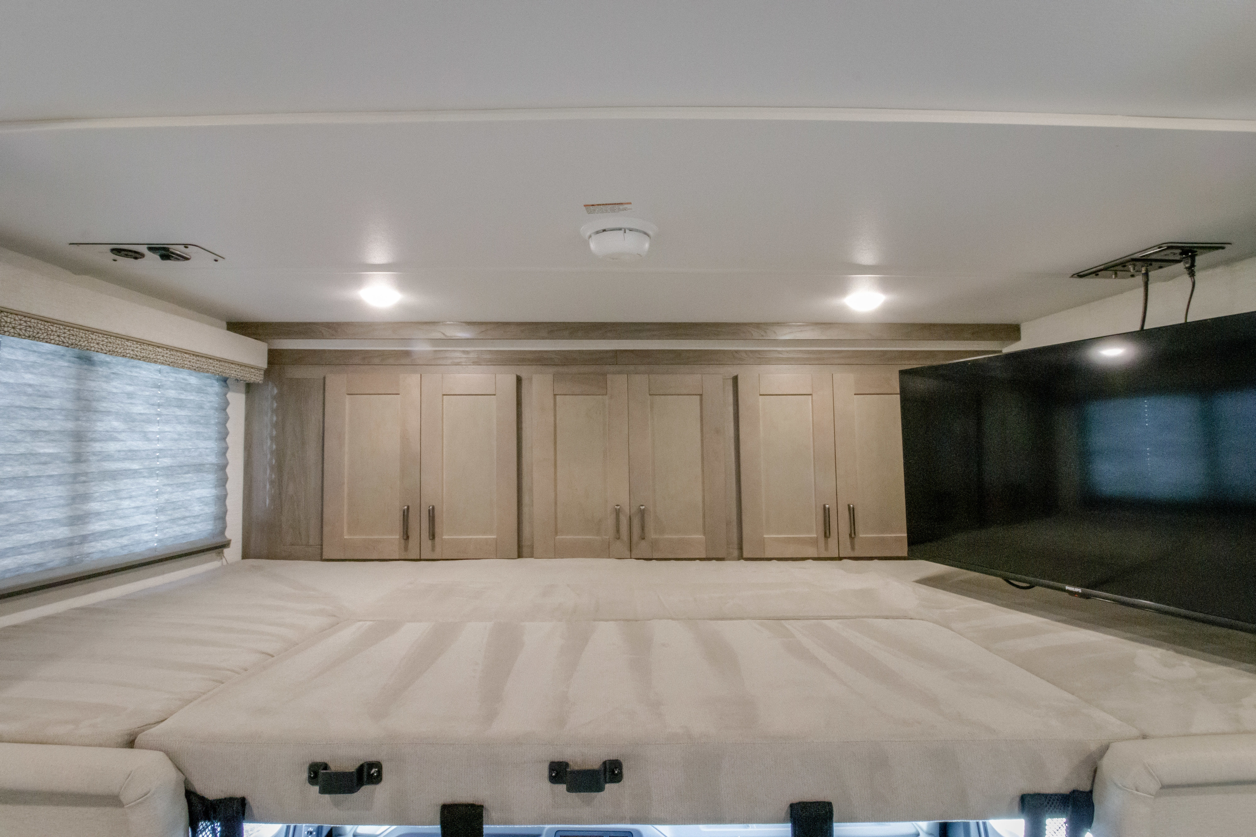 Cozy RV rental overhead bunk area features a plush bed, ample storage in wood cabinets, and a mounted TV for entertainment.. GULFSTREAM CONQUEST 2025
