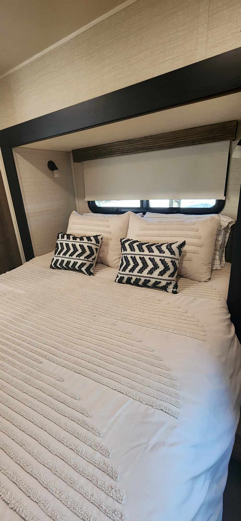 Cozy RV rental bedroom featuring a bed with textured white bedding, geometric throw pillows, and a window with a shade.. Jayco Redhawk 2017
