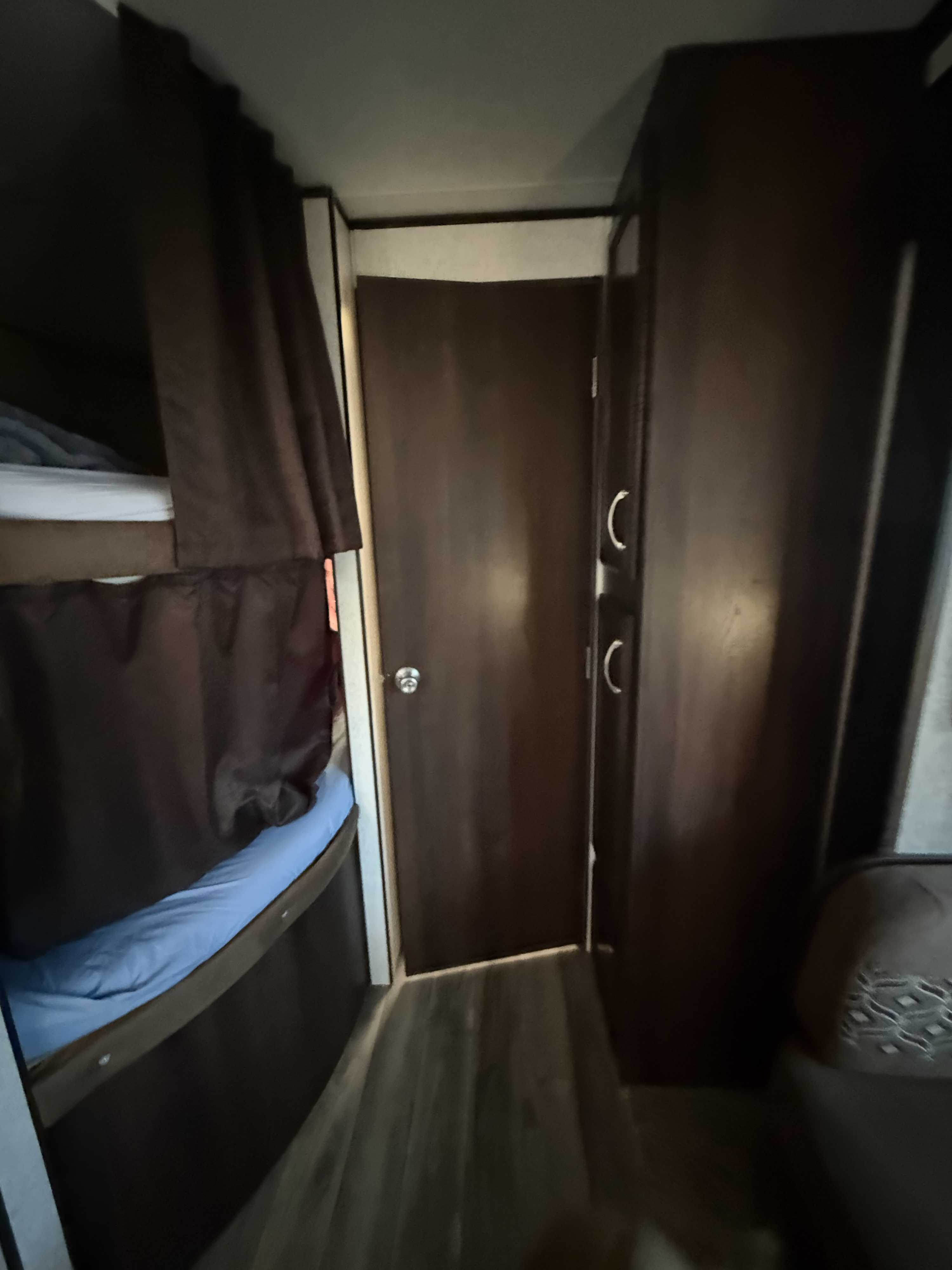 RV rental interior with bunk beds (blue sheet, brown curtains), a dark wood door, and a cabinet with silver handles.. Jayco Jay Flight 2018