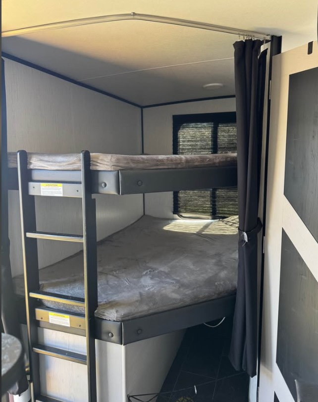 Cozy bunk beds with privacy curtain inside an RV rental, featuring a ladder and two comfortable mattresses for travelers.. Heartland RVs Mallard 2022
