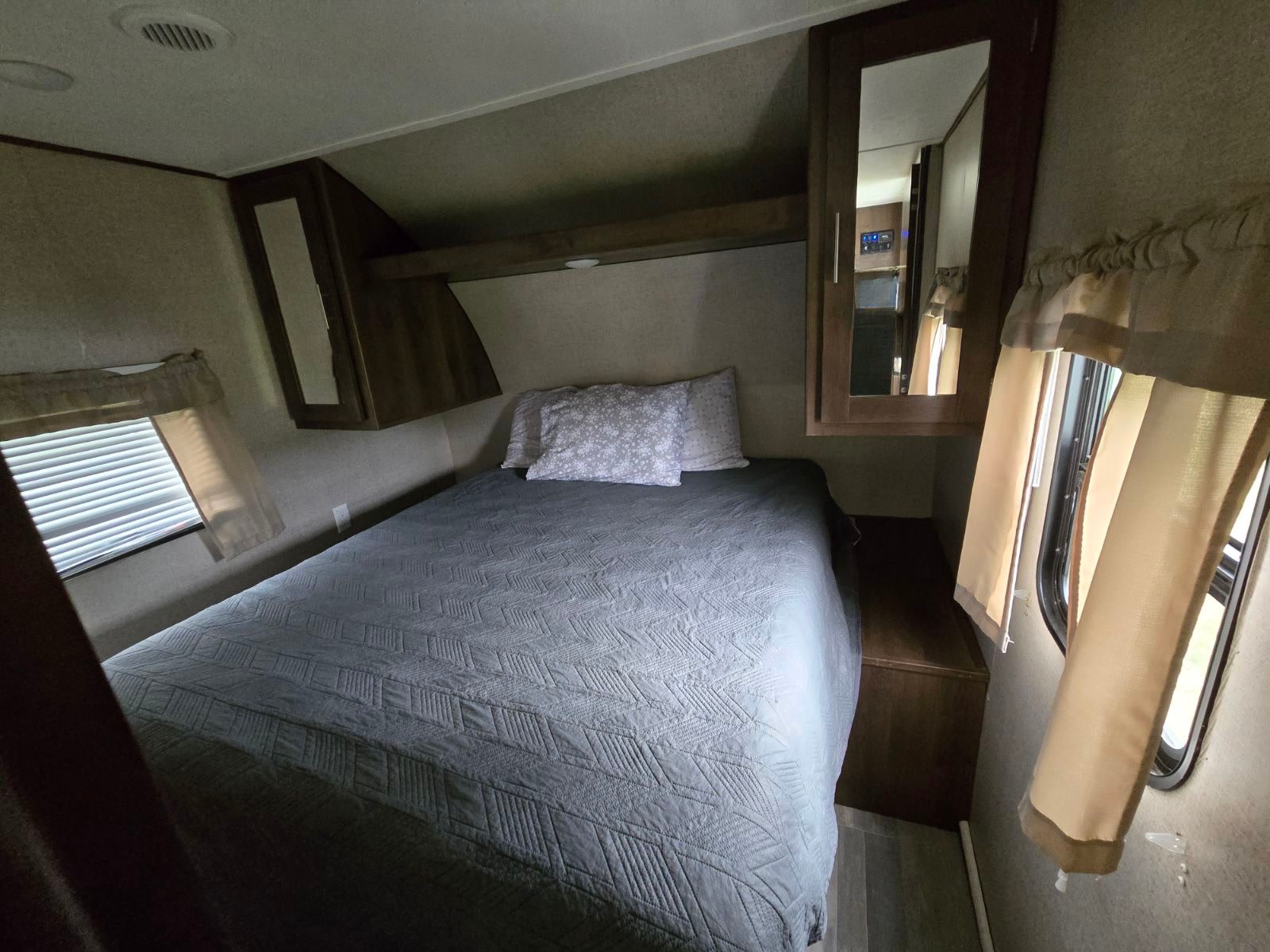 Comfortable RV rental bedroom featuring a gray bed, overhead storage, and windows with blinds.. Oasis 26BHS 2019