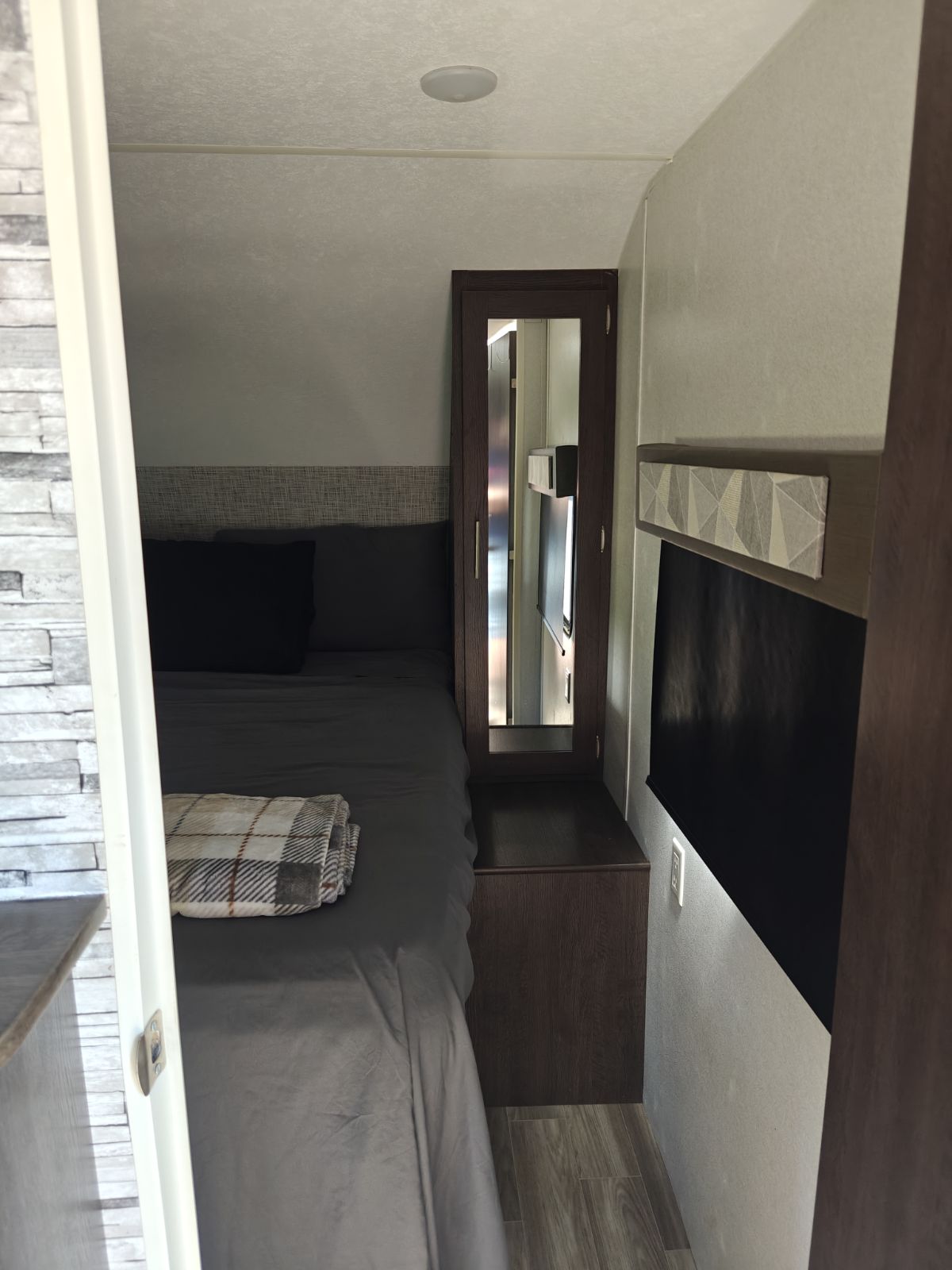 Cozy RV rental bedroom featuring a comfortable bed with gray linens, a plaid blanket, mirrored storage, and modern decor.. Salem 26DBUD 2020