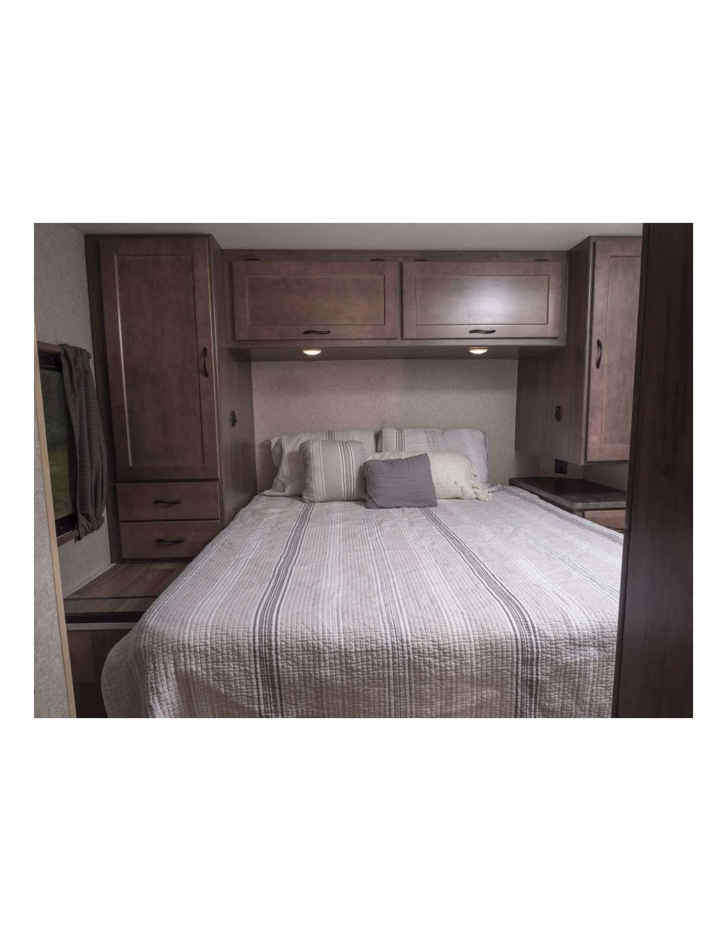 This RV rental bedroom has a comfortable bed with striped bedding, overhead and side cabinets, and warm accent lighting.. Winnebago 328QR 2020