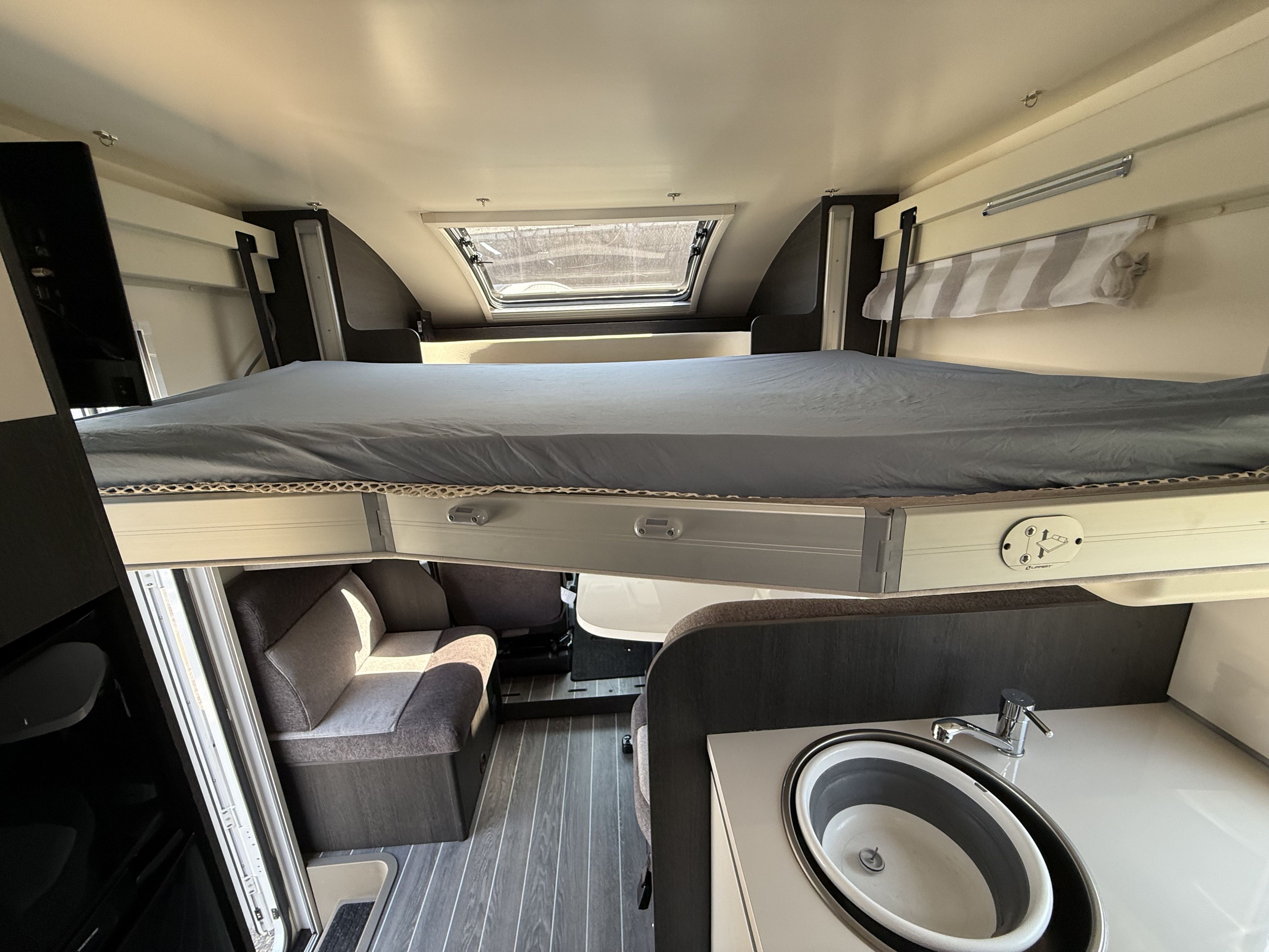 RV rental interior: overhead bed over seating area, with a kitchenette and sink visible on the right.. Rollerteam Zefiro 696 2025