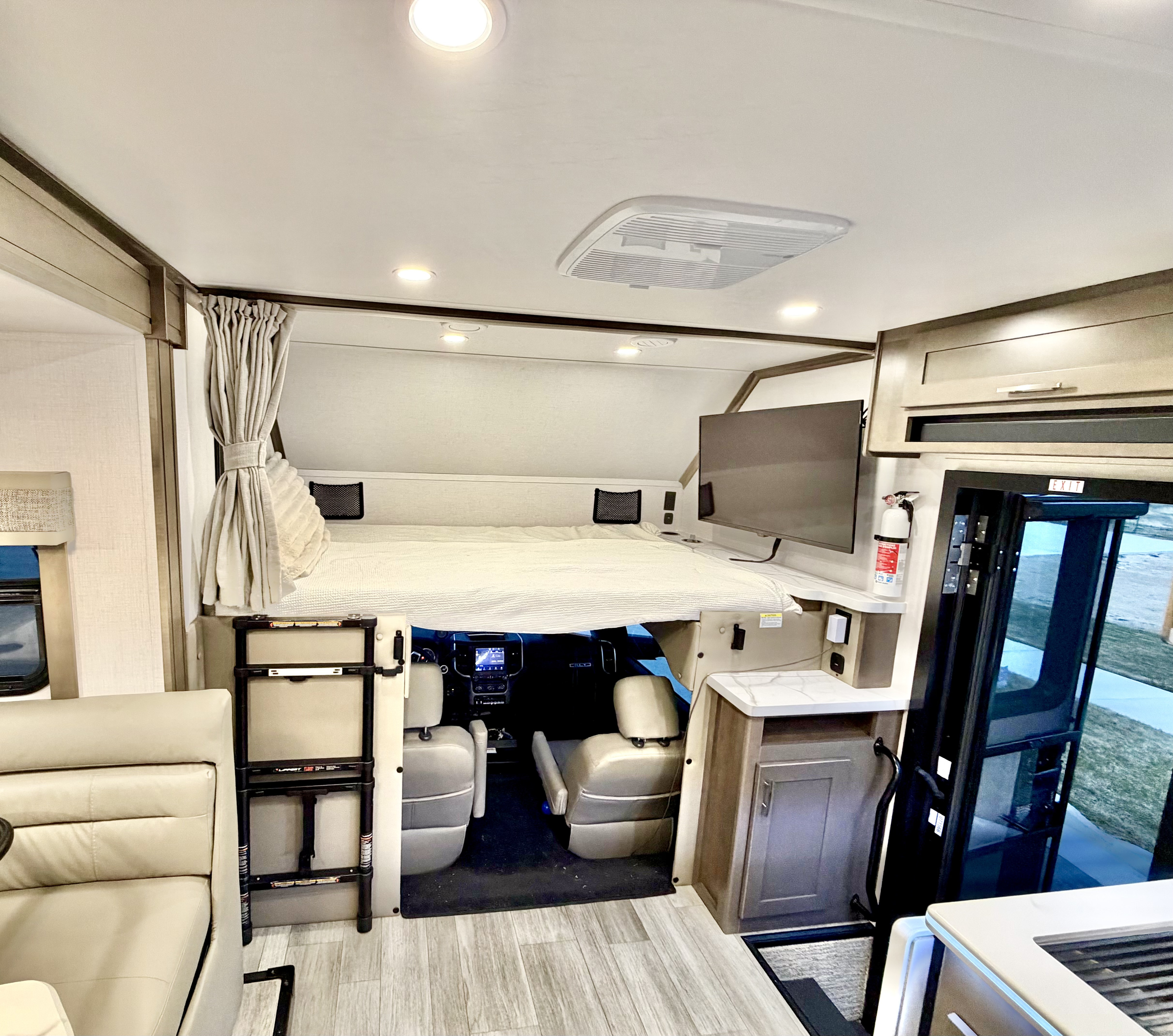 Interior of an RV rental featuring a cab-over bed, modern living space, and driver's area, with an entry door visible.. Dynamax Explore ISATA 5 Explorer Extreme Package 2026