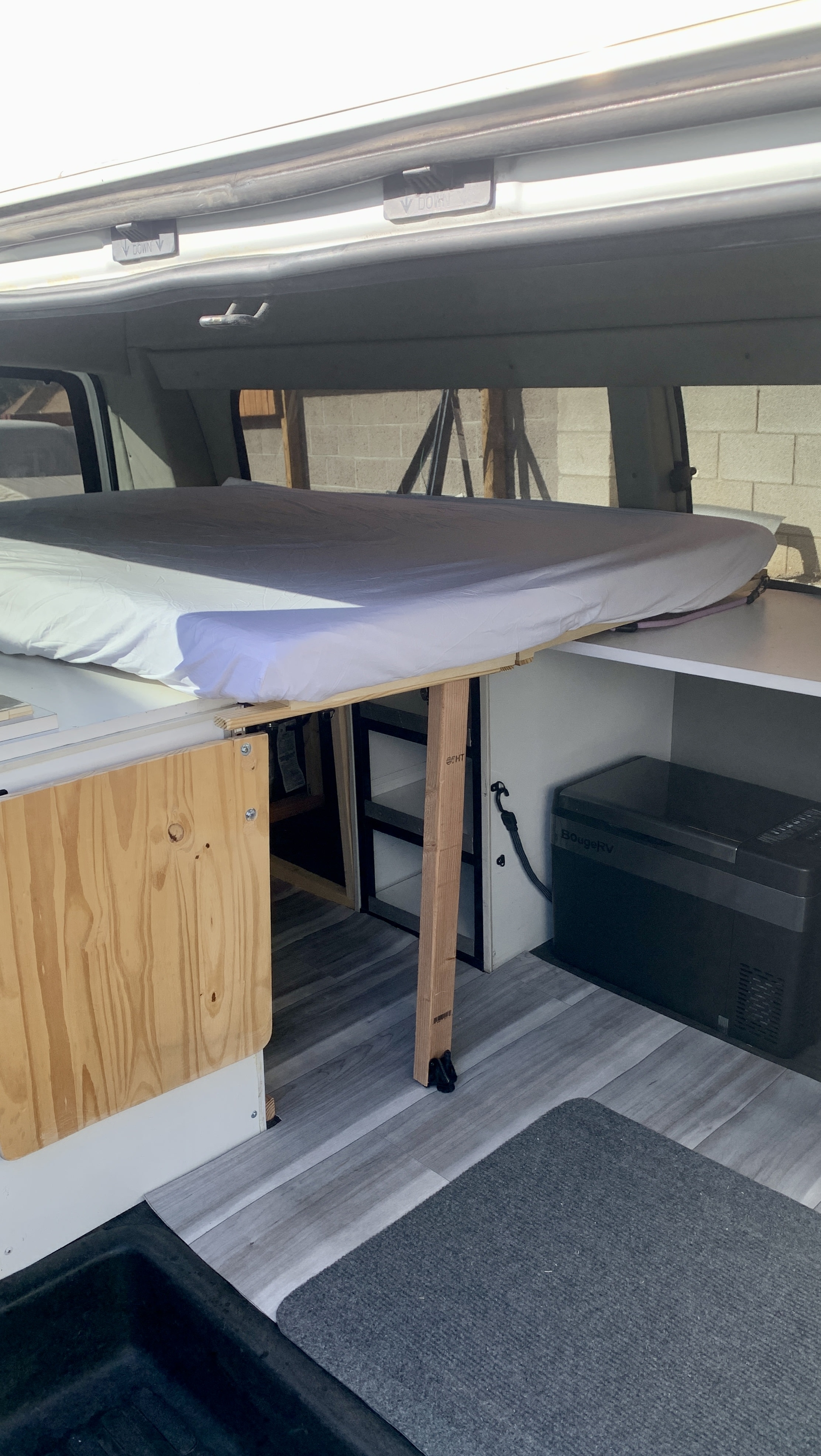 RV rental: Cozy camper van interior featuring a custom-built bed, portable fridge, and smart storage for comfortable travel.. Chevrolet Express 2011