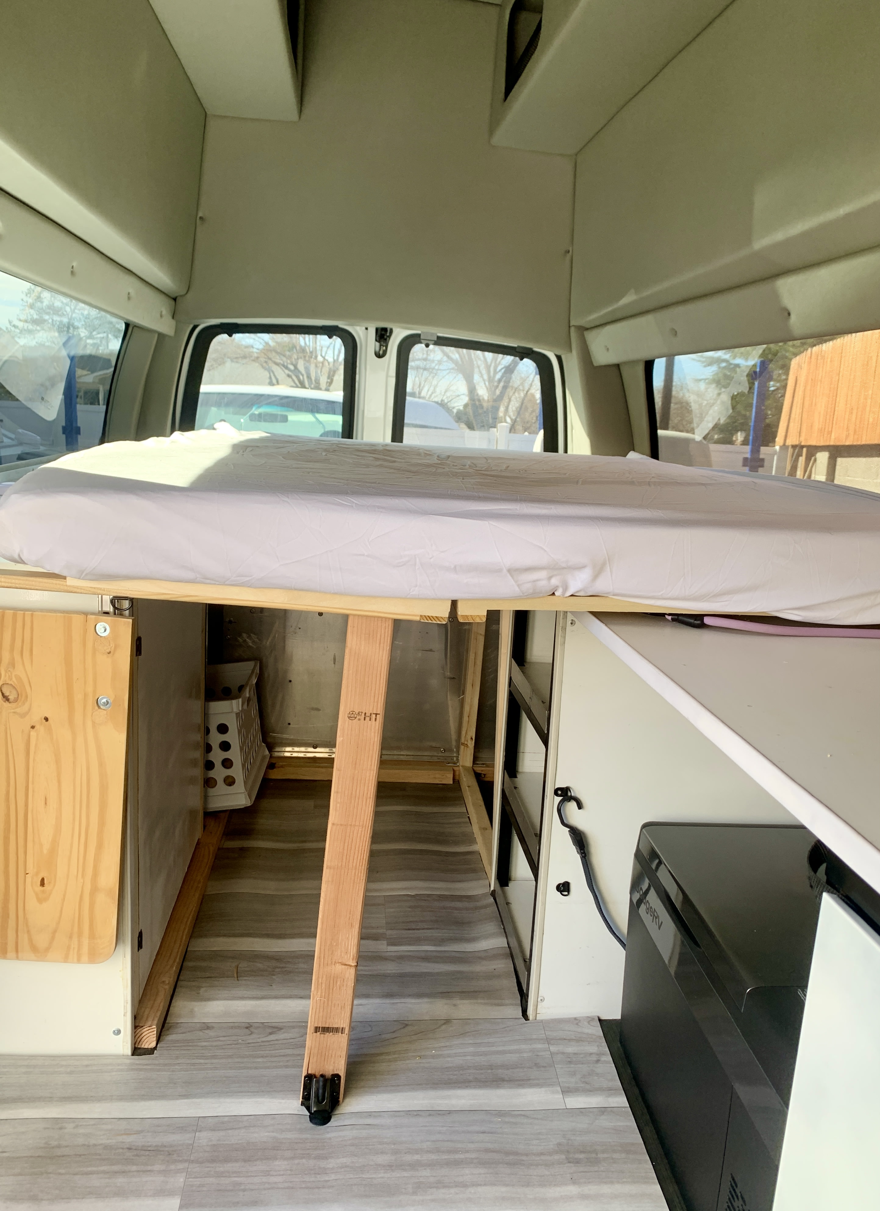 Inside an RV rental camper van: raised bed, under-bed storage, and a portable fridge, showcasing travel-ready comfort.. Chevrolet Express 2011