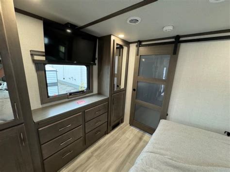Spacious RV rental bedroom featuring a mounted TV, ample storage drawers, and a stylish sliding barn door.. Grand Design Solitude 2024