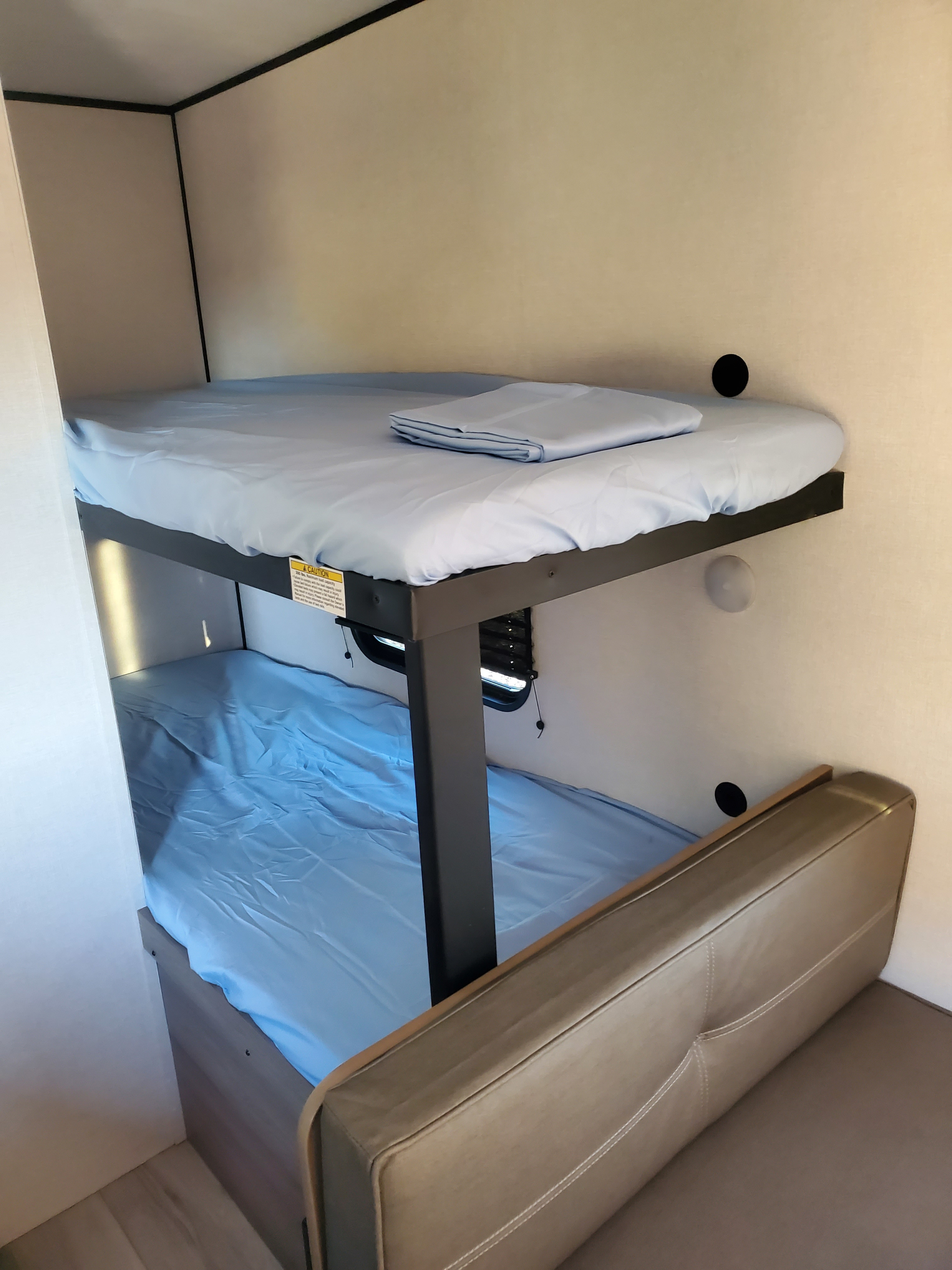 Cozy RV rental bunk beds with light blue sheets & a tan sleeper sofa provide comfortable sleeping arrangements.. Keystone RV Coleman 2026