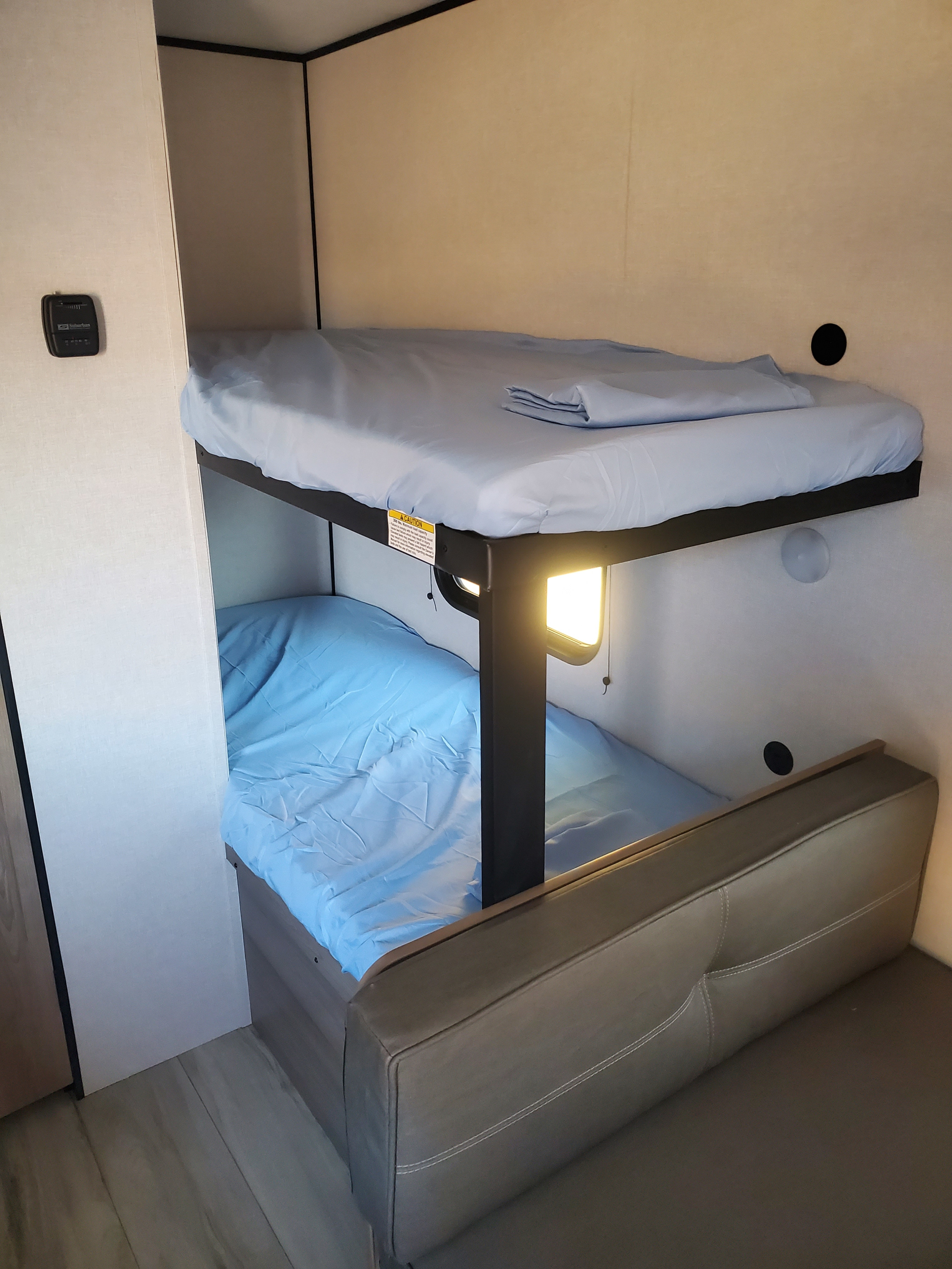 Cozy RV rental bunk beds with light blue sheets and a sofa, perfect for comfortable accommodation during travel.. Keystone Coleman 2026