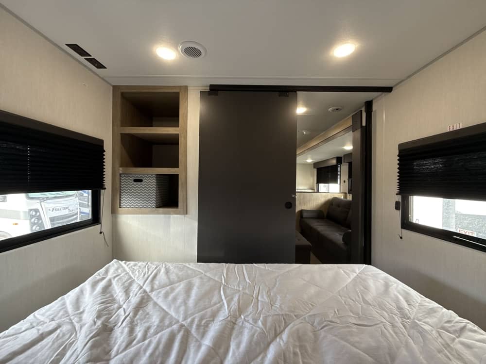 Cozy RV rental bedroom with a comfy bed, shelves, and a sliding door leading to the living area with a couch.. Forest River Campsite Reserve 26CJ 2026