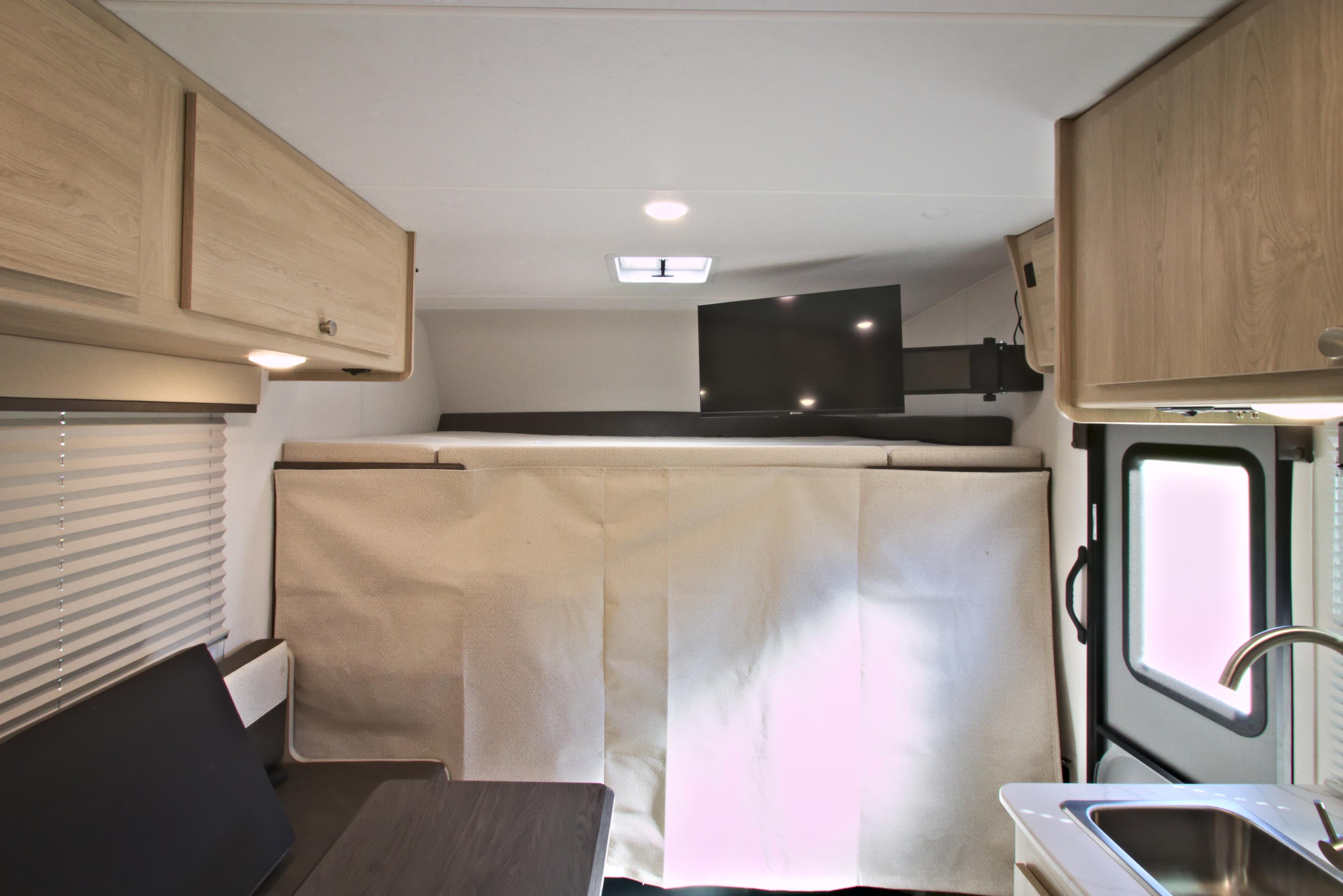 Interior of an rv rental with a bunk bed, mounted TV, kitchen sink, light-colored overhead cabinets, and a window with blinds.. Forest River Coachmen Leprechaun SS 2026