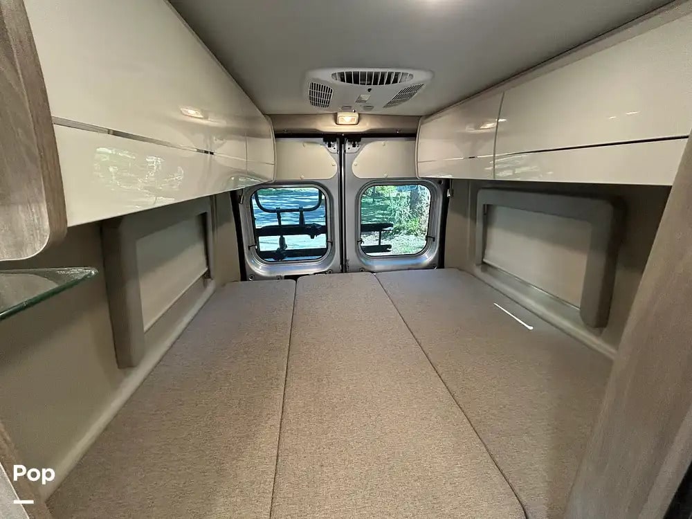 Spacious rv rental interior featuring a comfortable bed, overhead storage, and windows looking out to nature. Perfect for travel.. Thor Tellaro 2023