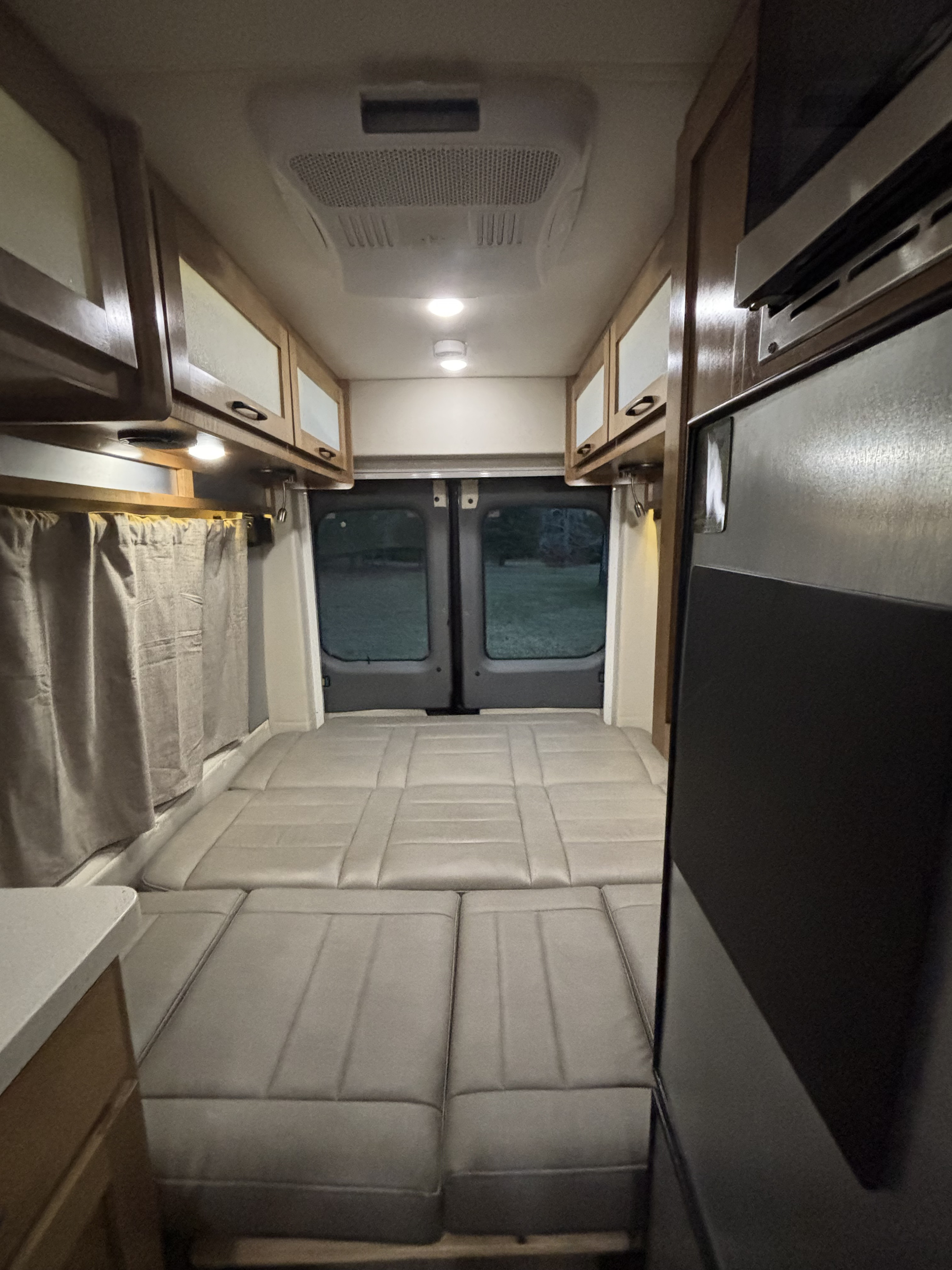 Spacious rv rental interior featuring a convertible bed, overhead cabinets, and kitchen appliances, looking towards the rear doors.. Coachmen Beyond 22C 2020