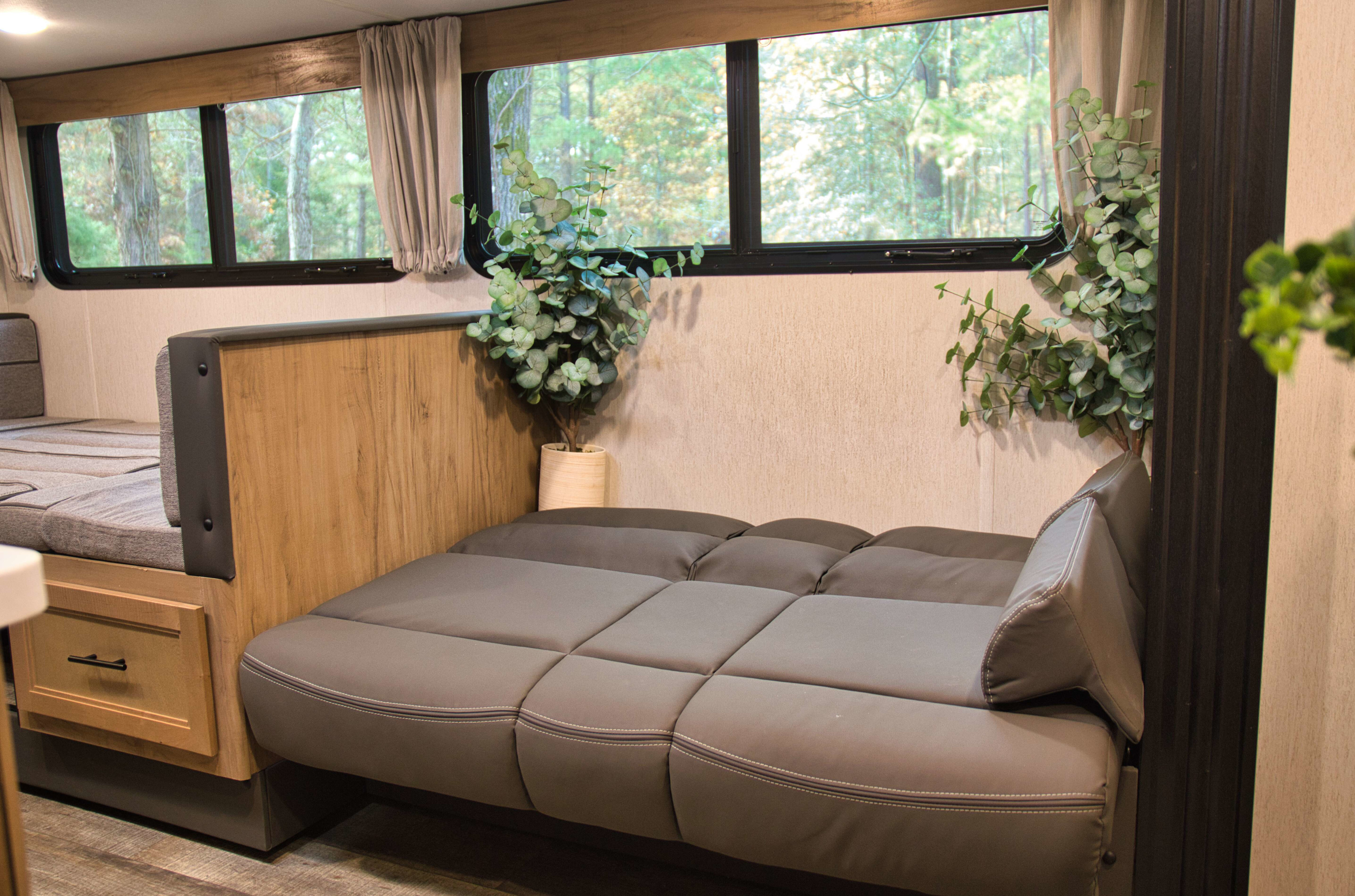 Cozy RV rental interior with comfortable seating, a convertible bed, and large windows revealing a scenic forest view.. Forest River Cherokee Grey Wolf 2023