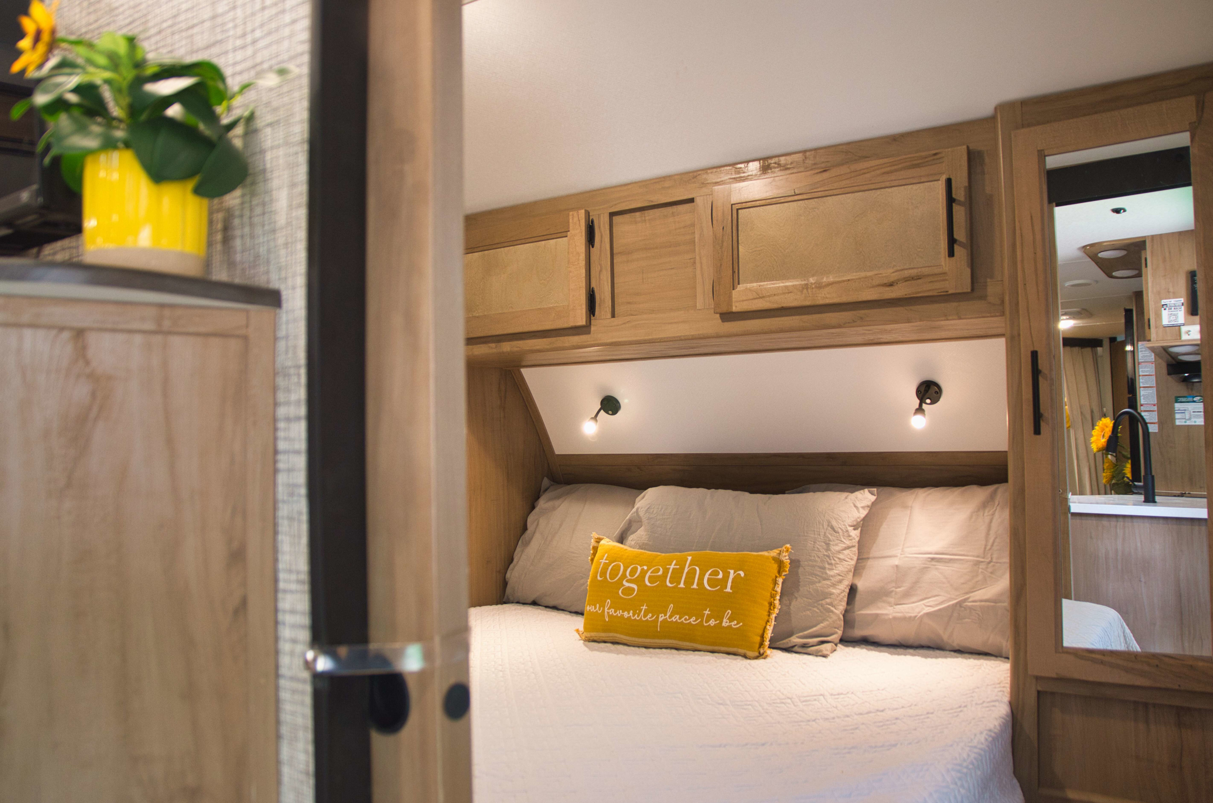 Cozy RV rental bedroom with a bed, yellow accent pillow "together", overhead cabinets, and reading lights, perfect for travel.. Forest River Cherokee Grey Wolf 2023