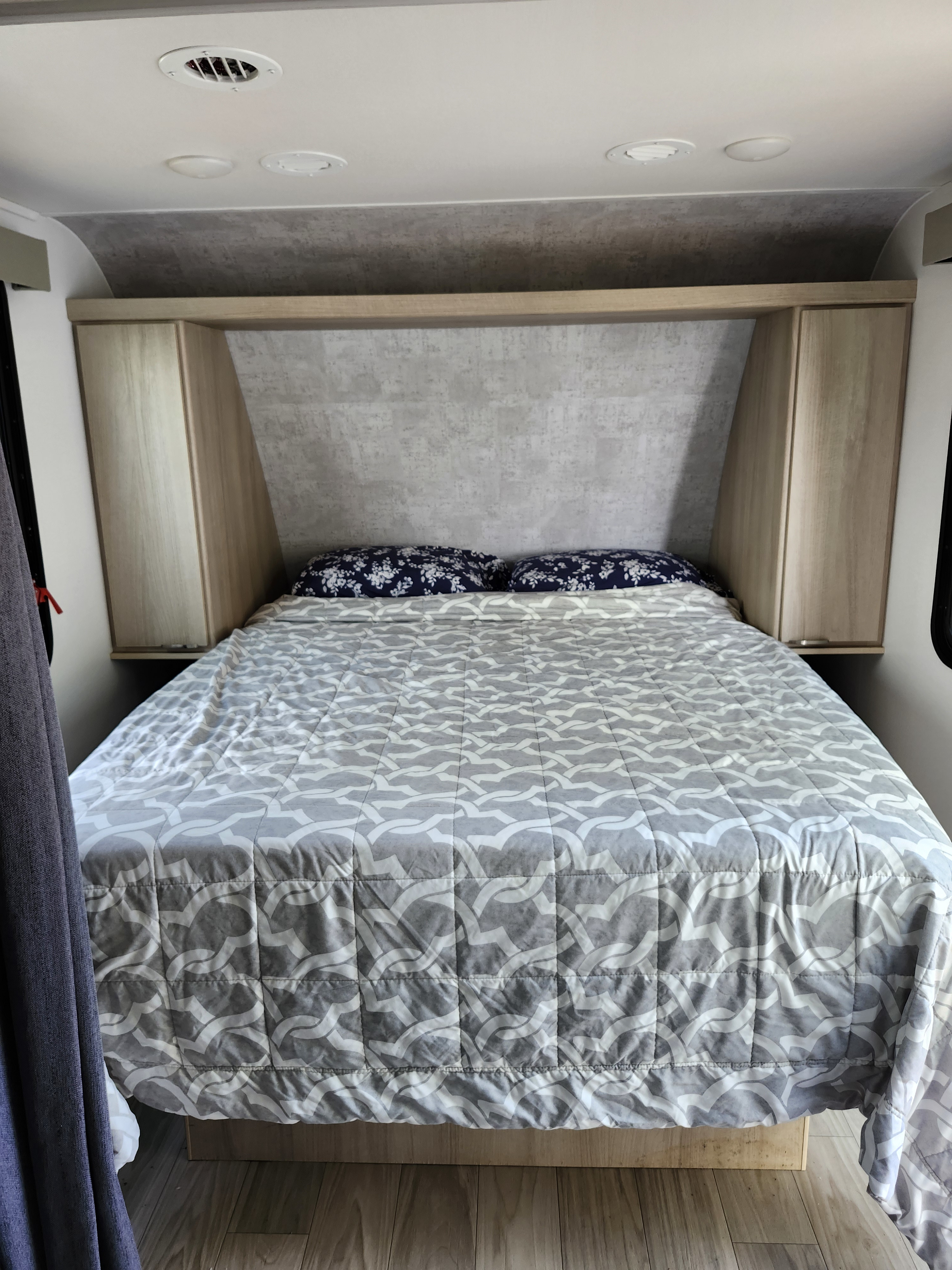 RV rental bedroom featuring a comfortable bed with a patterned comforter, floral pillows, and overhead storage.. Winnebago Minnie Winnie 2025