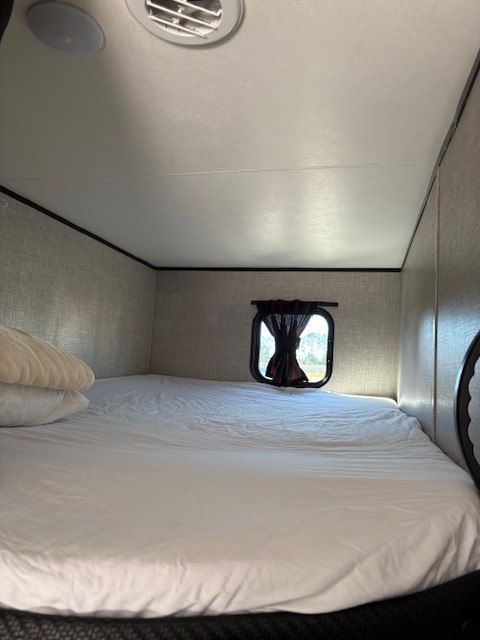 This cozy RV rental bunk bed features white sheets, pillows, a small window, and ceiling vents, perfect for travel.. Jayco Jay Flight 2022