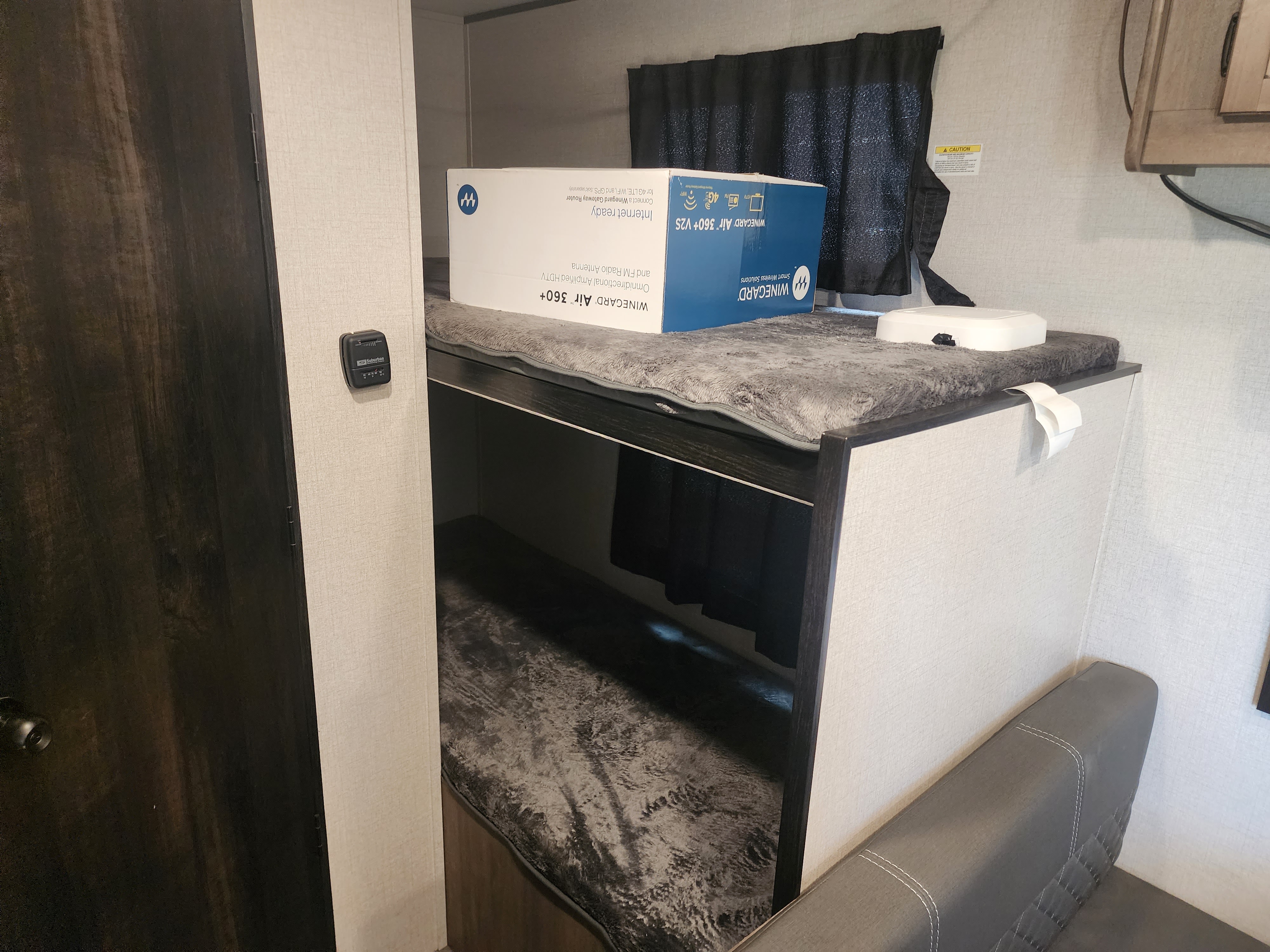 Inside an RV rental: bunk beds, a Winegard Air 360+ box on top, wall thermostat, and dark door.. Highland Ridge RV Olympia Sport 2022