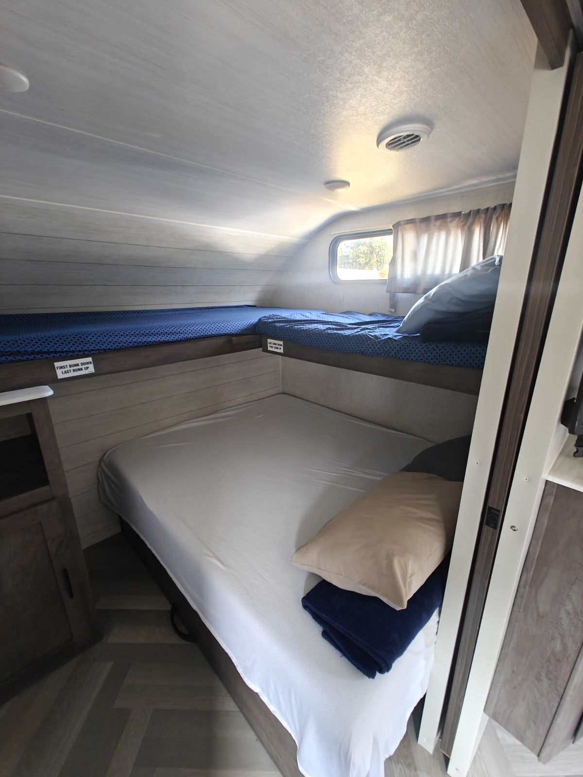 Spacious RV rental sleeping area featuring three bunk beds with blue and white bedding, a window, and wood-look walls.. Salem 36VBDS 2021