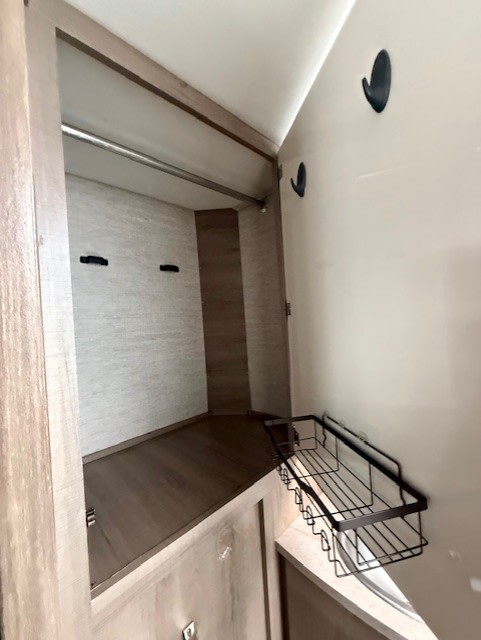 RV rental closet featuring a hanging rod, hooks, bottom shelf, and a black wall-mounted storage basket.. Jayco Melbourne Prestige 2023