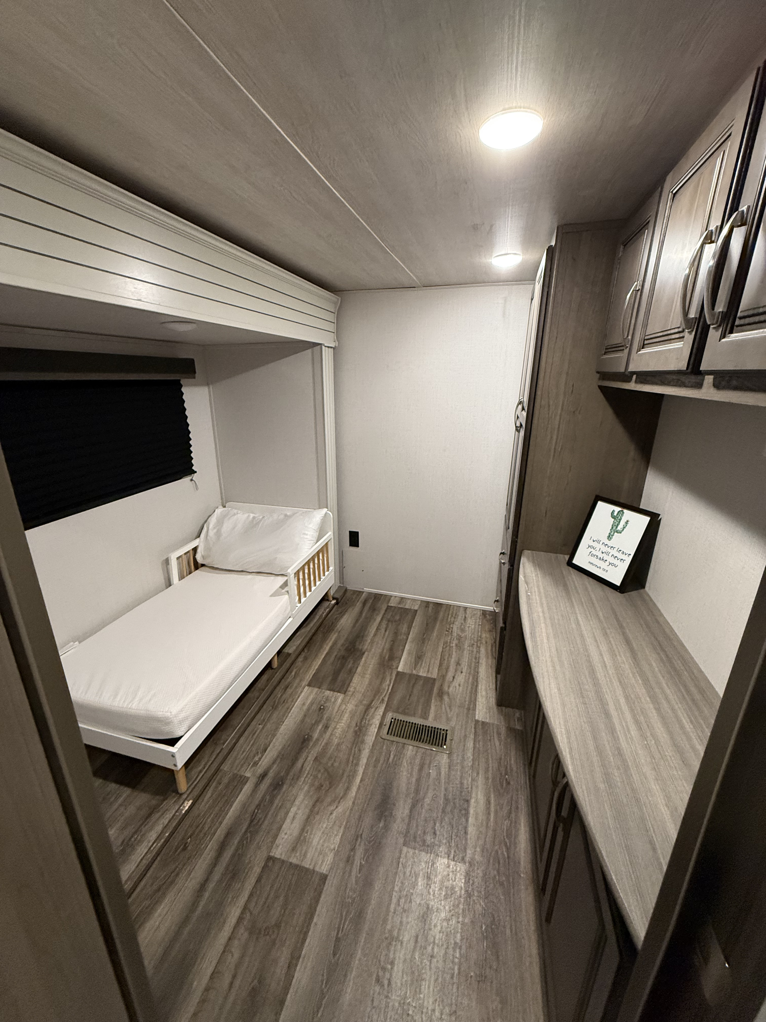 RV rental's cozy sleeping area: a child's bed, window with blind, wood-look floor, and storage cabinets.. Keystone RV Cougar 2021