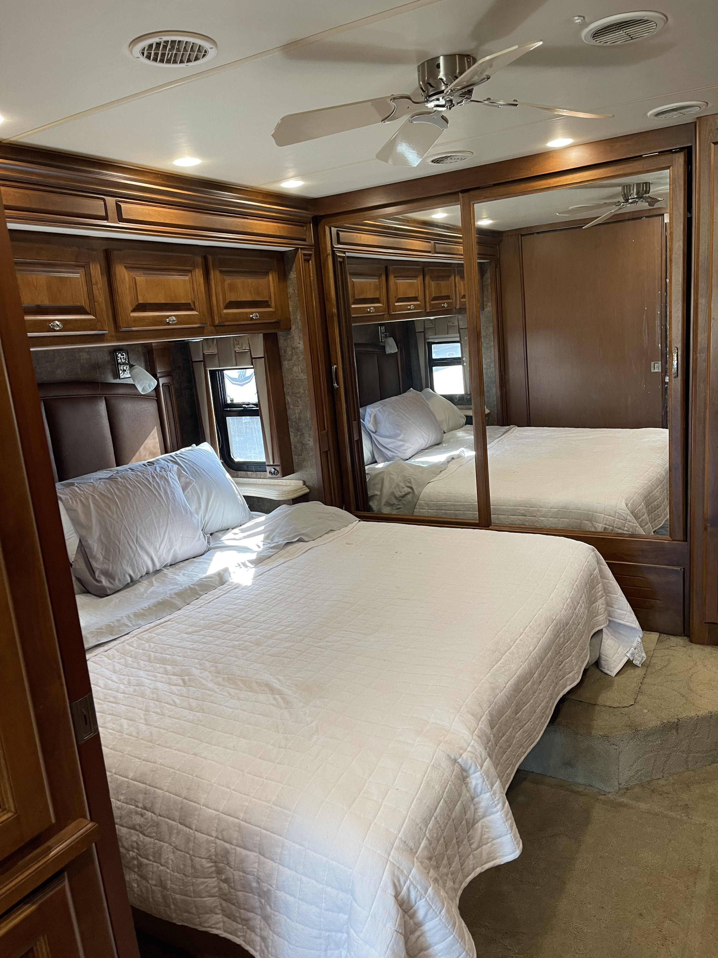 RV rental: Bedroom with a spacious bed, white bedding, mirrored wardrobe, wood cabinets, and ceiling fan.. Phaeton Phaeton Motorhome 2011