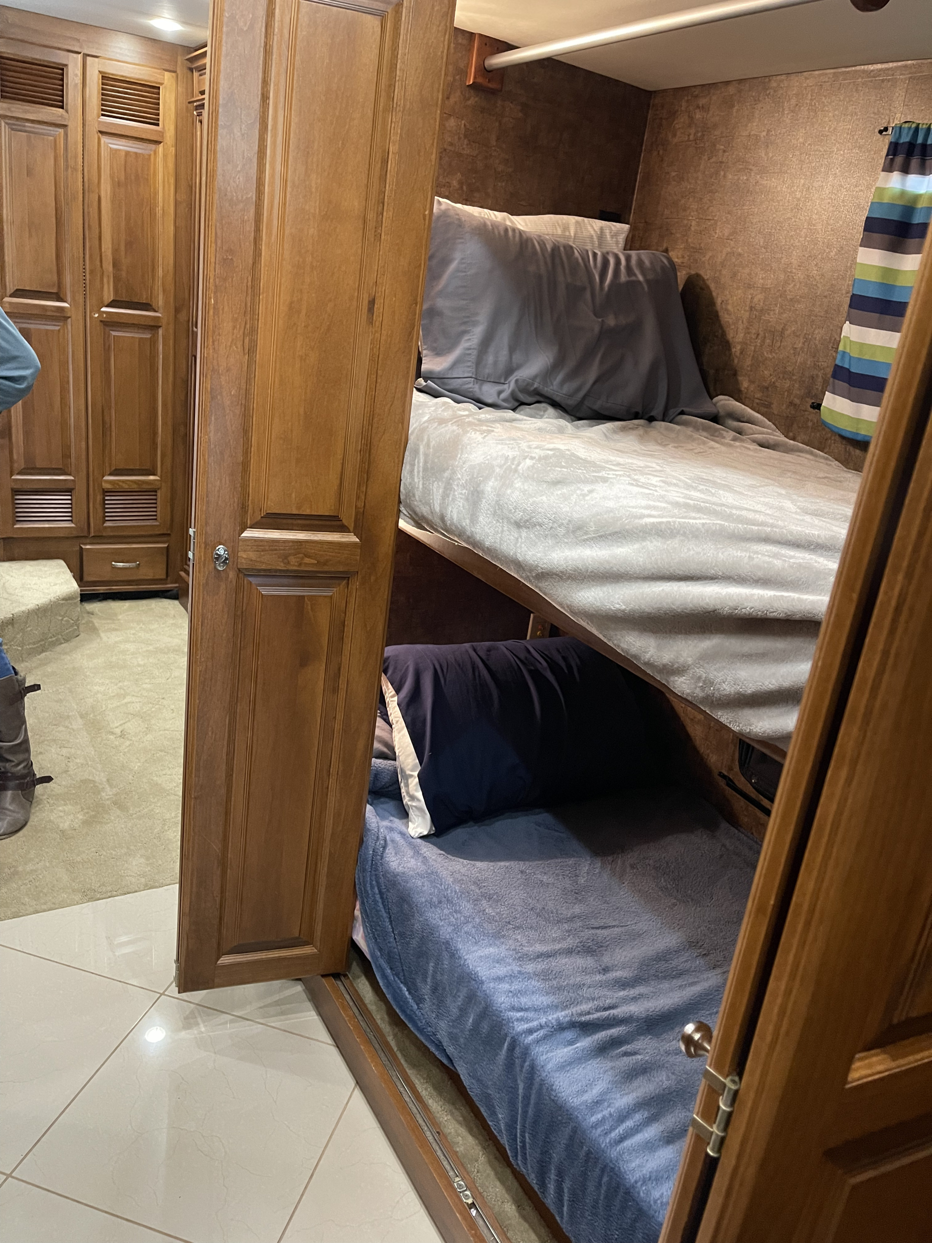 Cozy RV rental bunk beds with warm wooden cabinetry offer sleeping space. Plush bedding & colorful curtains enhance comfort.. Phaeton Phaeton Motorhome 2011