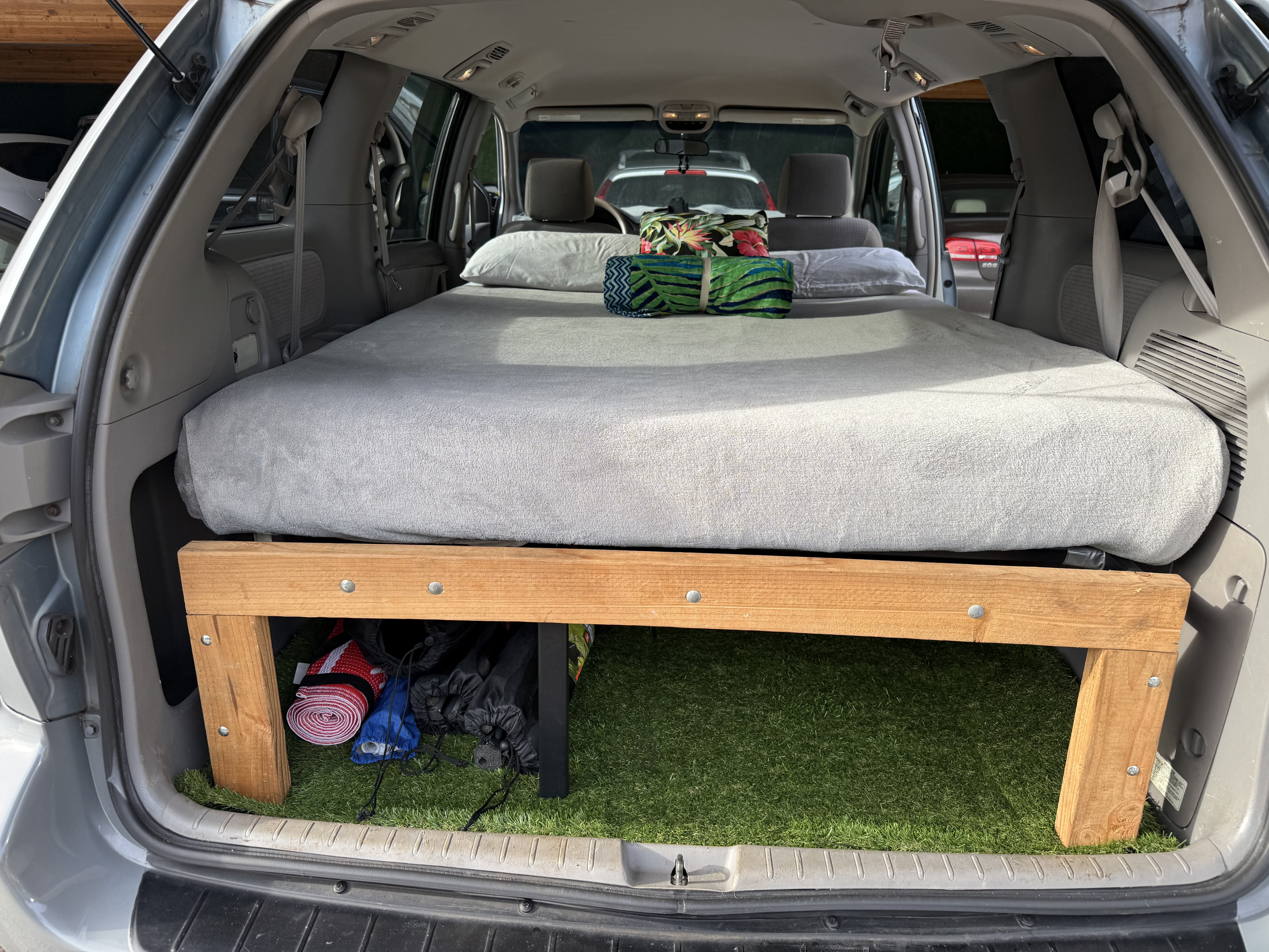 RV rental ready: van interior with a custom bed platform, mattress, pillows, and artificial turf storage underneath.. Toyota Sienna 2006