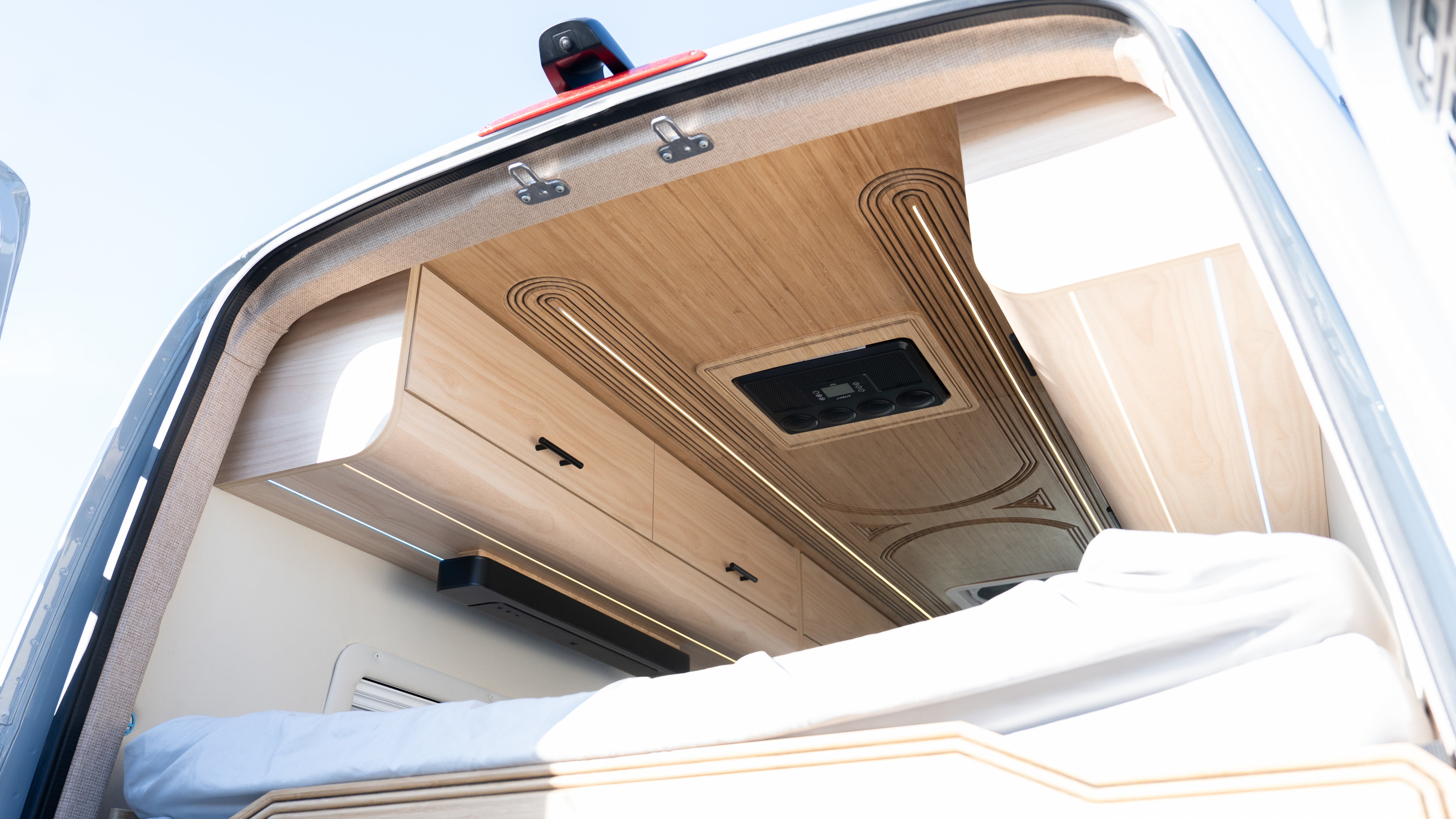 Upward view inside a modern rv rental camper: light wood ceiling, ambient lighting, overhead cabinets, and controls above a comfy bed.. Other Mercedes Sprinter 2024