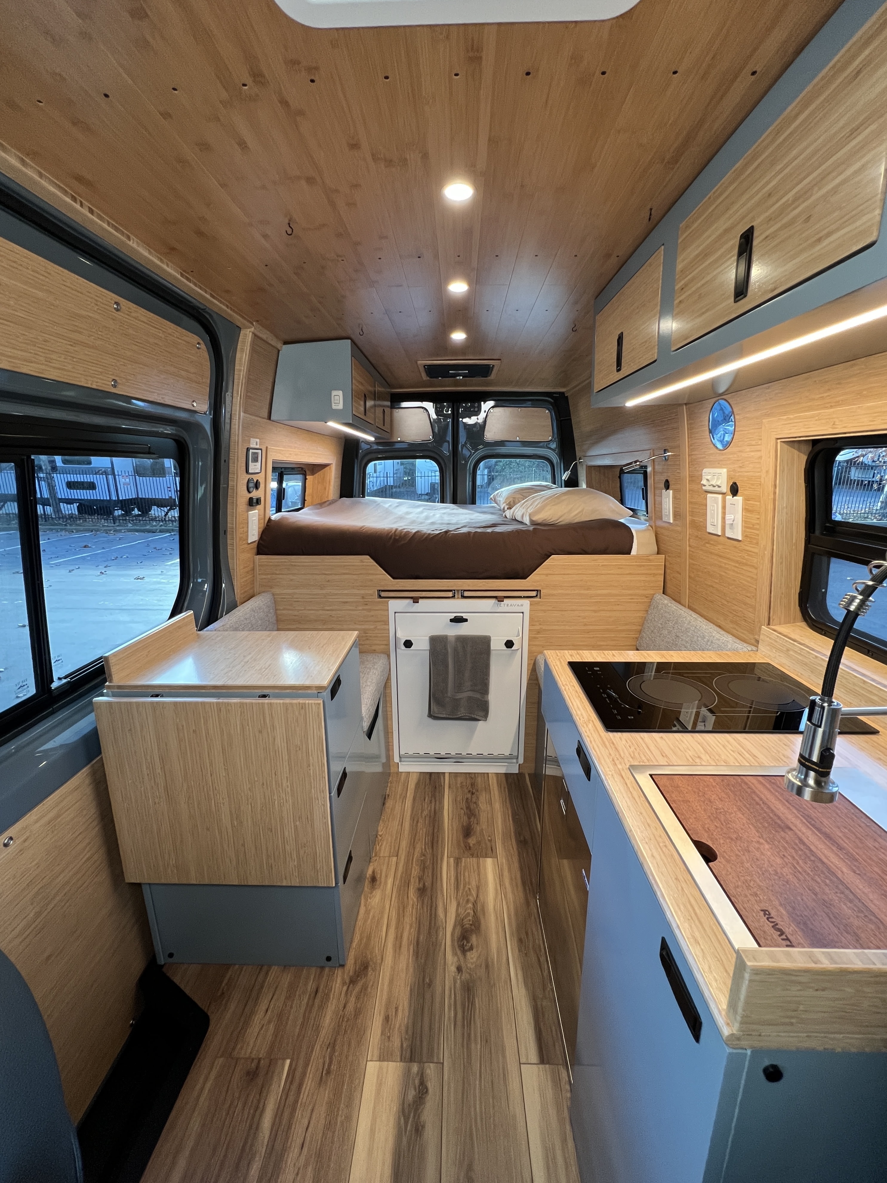 Modern rv rental camper van interior featuring a cozy bed, compact kitchen, and warm wood finishes.. Mercedes-Benz Sprinter 2024