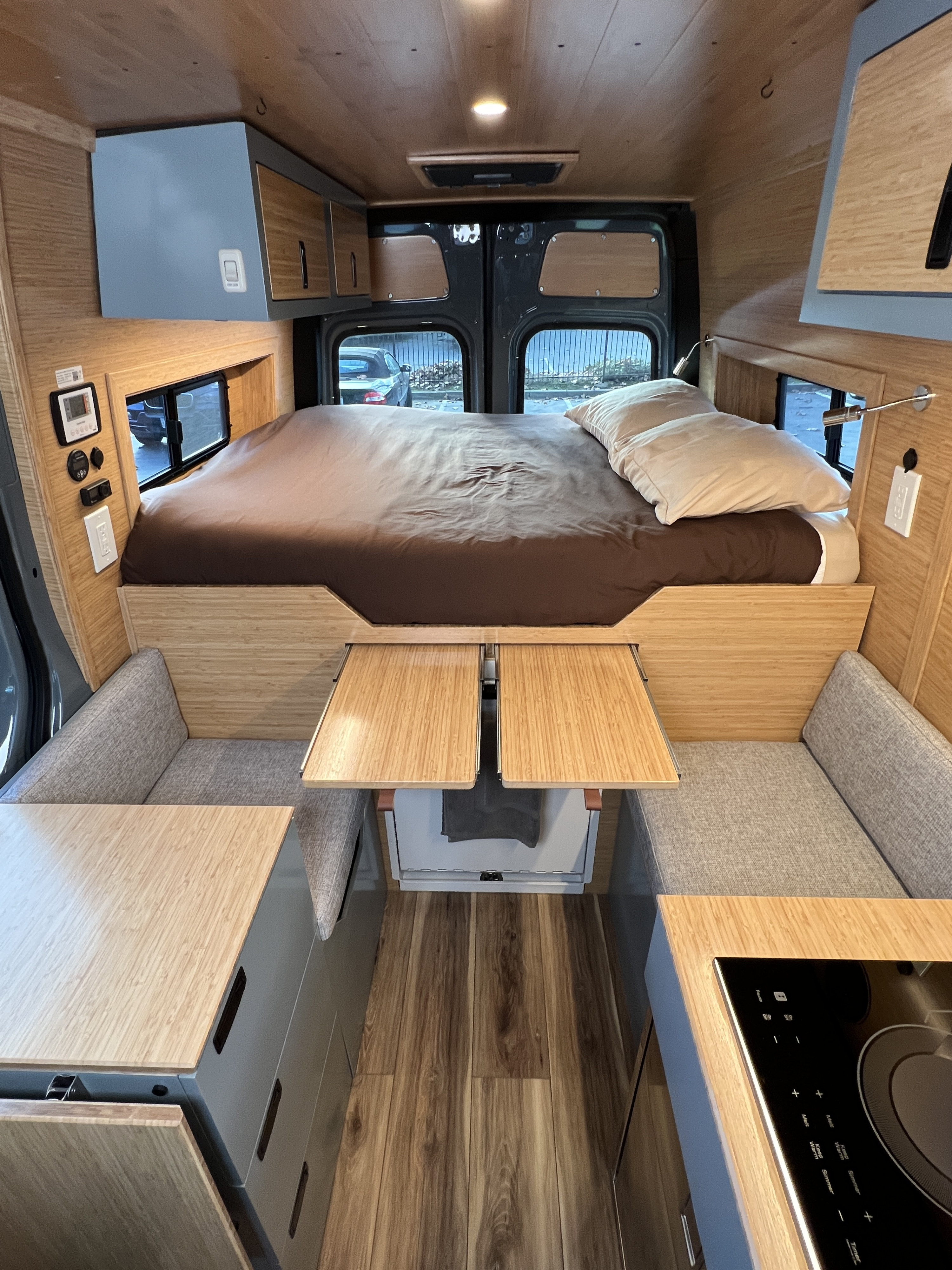 RV rental: Modern camper van interior with a bed, bench seating, foldable tables, and an induction cooktop kitchen.. Mercedes-Benz Sprinter 2024