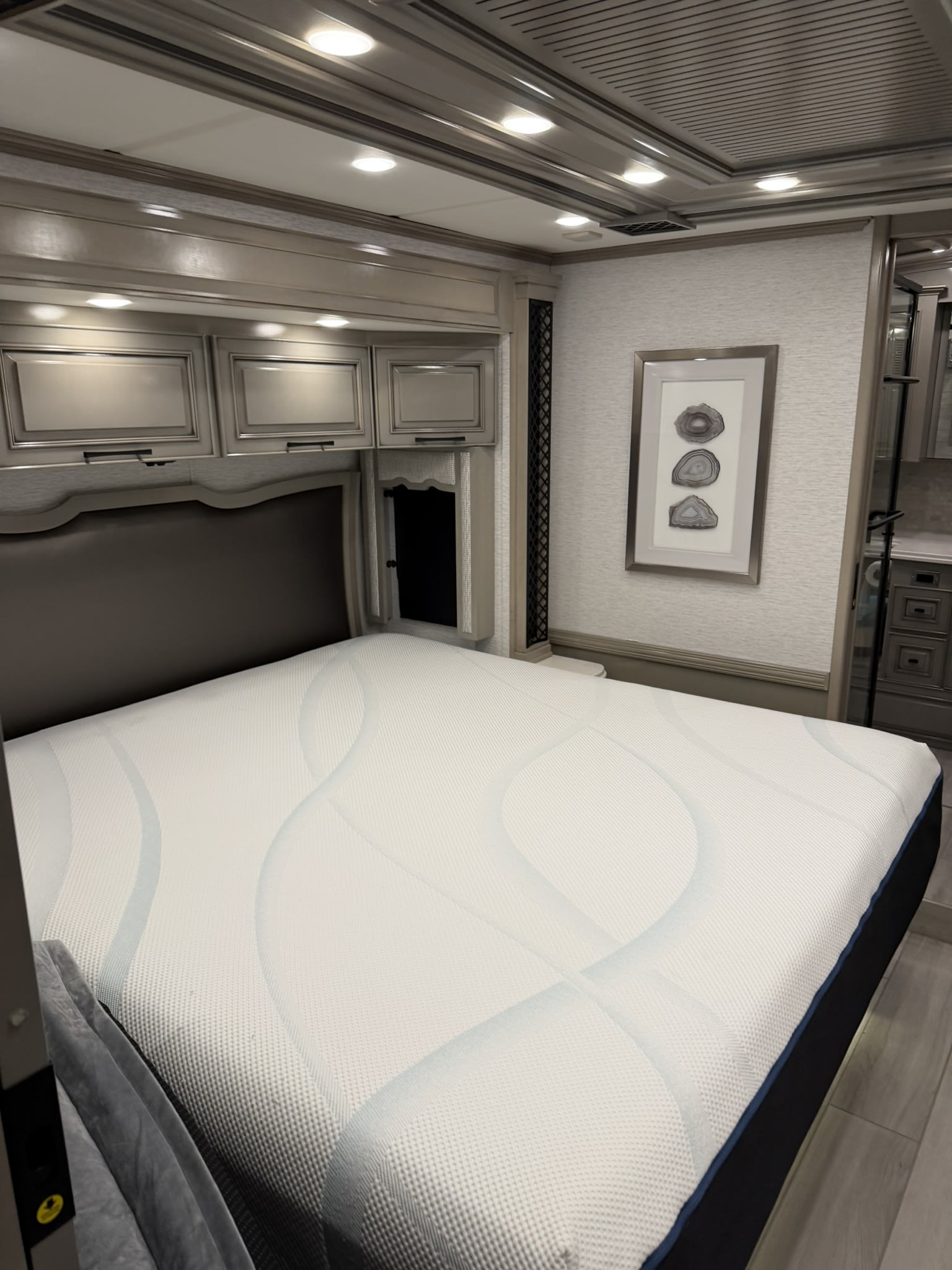 Inside an RV rental: a modern bedroom with a comfortable white mattress, dark upholstered headboard, and elegant overhead storage.. London Aire London Aire Motorhome 2024