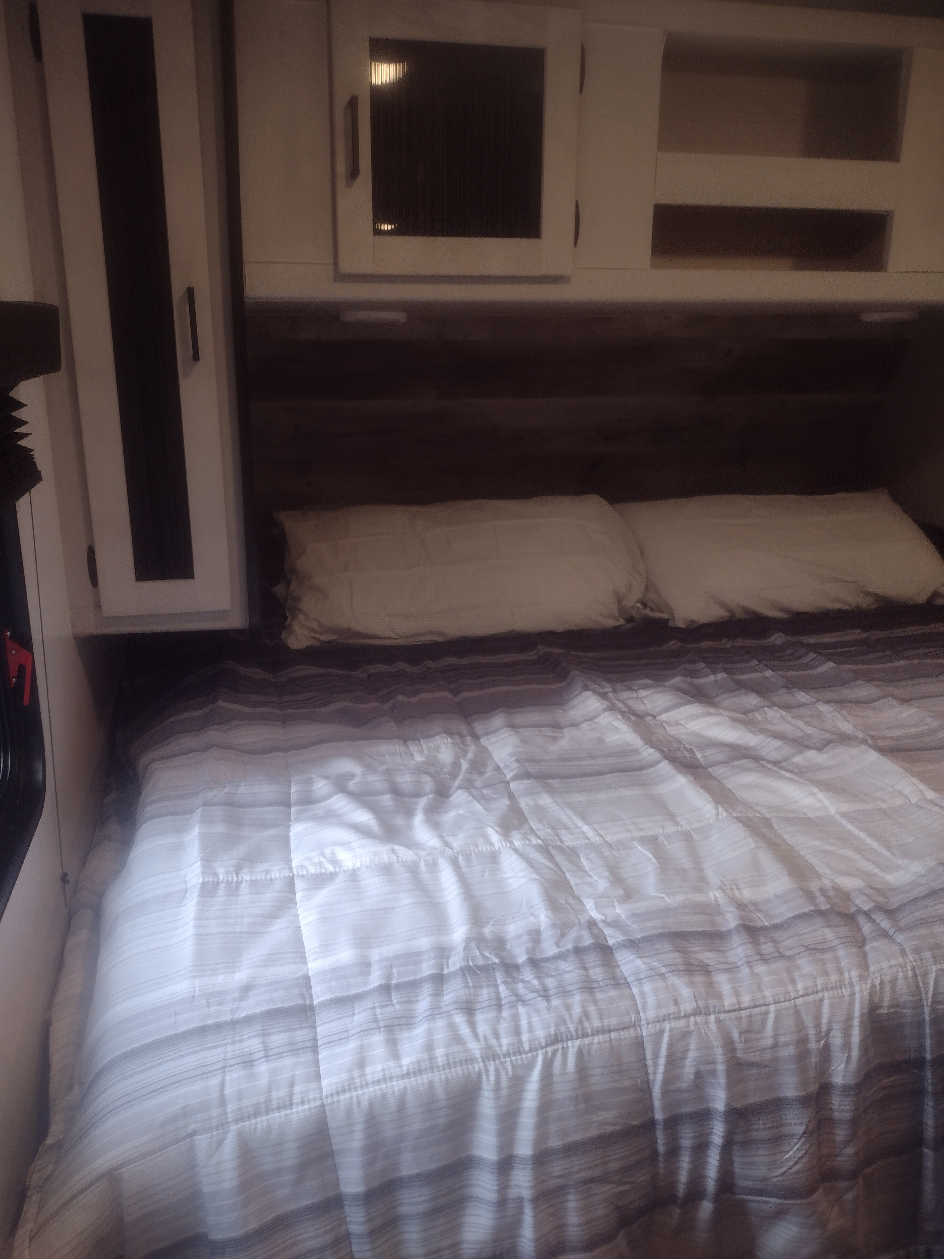 Cozy RV rental bedroom with a striped comforter, pillows, and overhead storage cabinets, ready for your next adventure.. Heartland RVs Mallard 2022